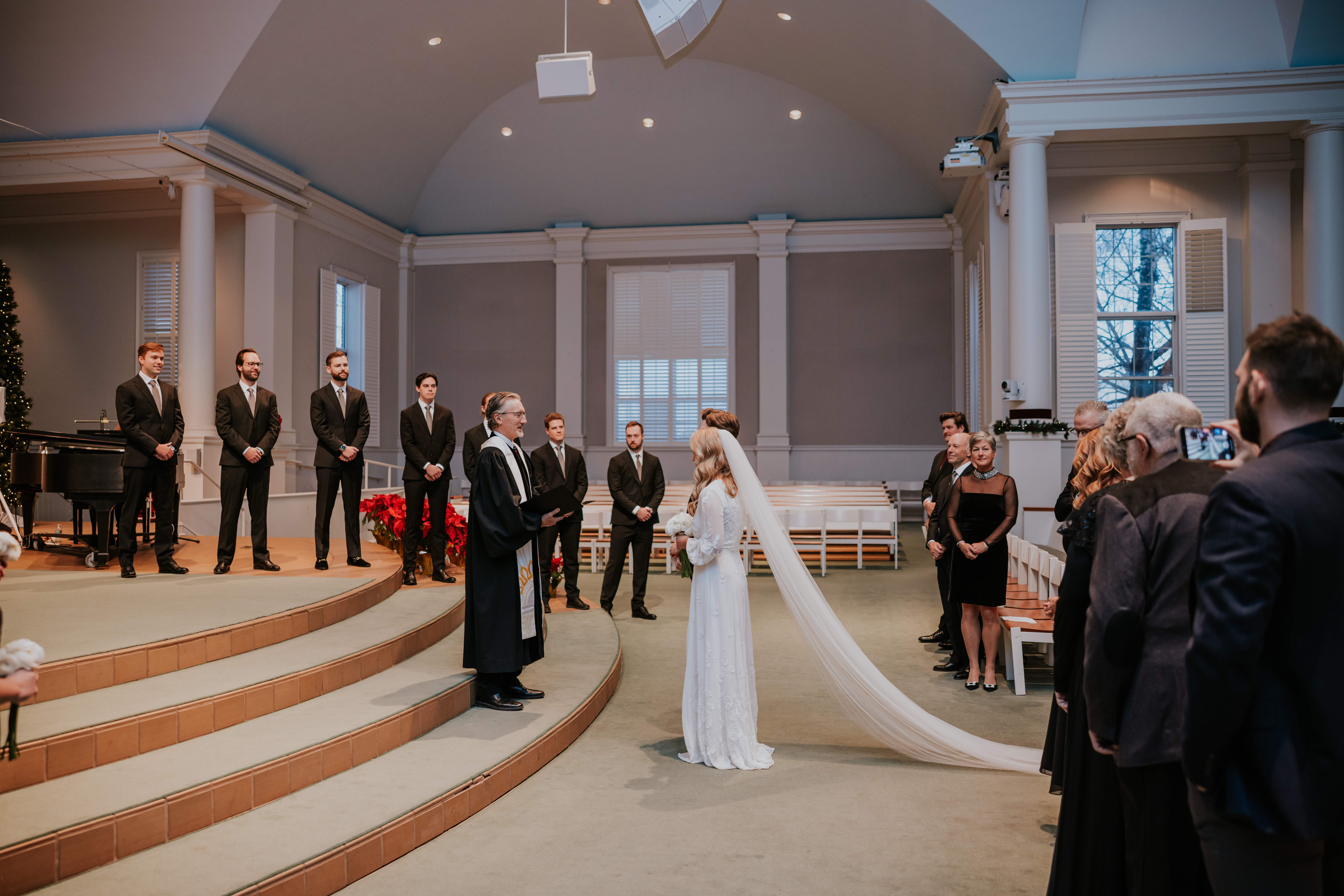 Wedding ceremony with the bride and groom standing before the officiant and wedding party in a church.