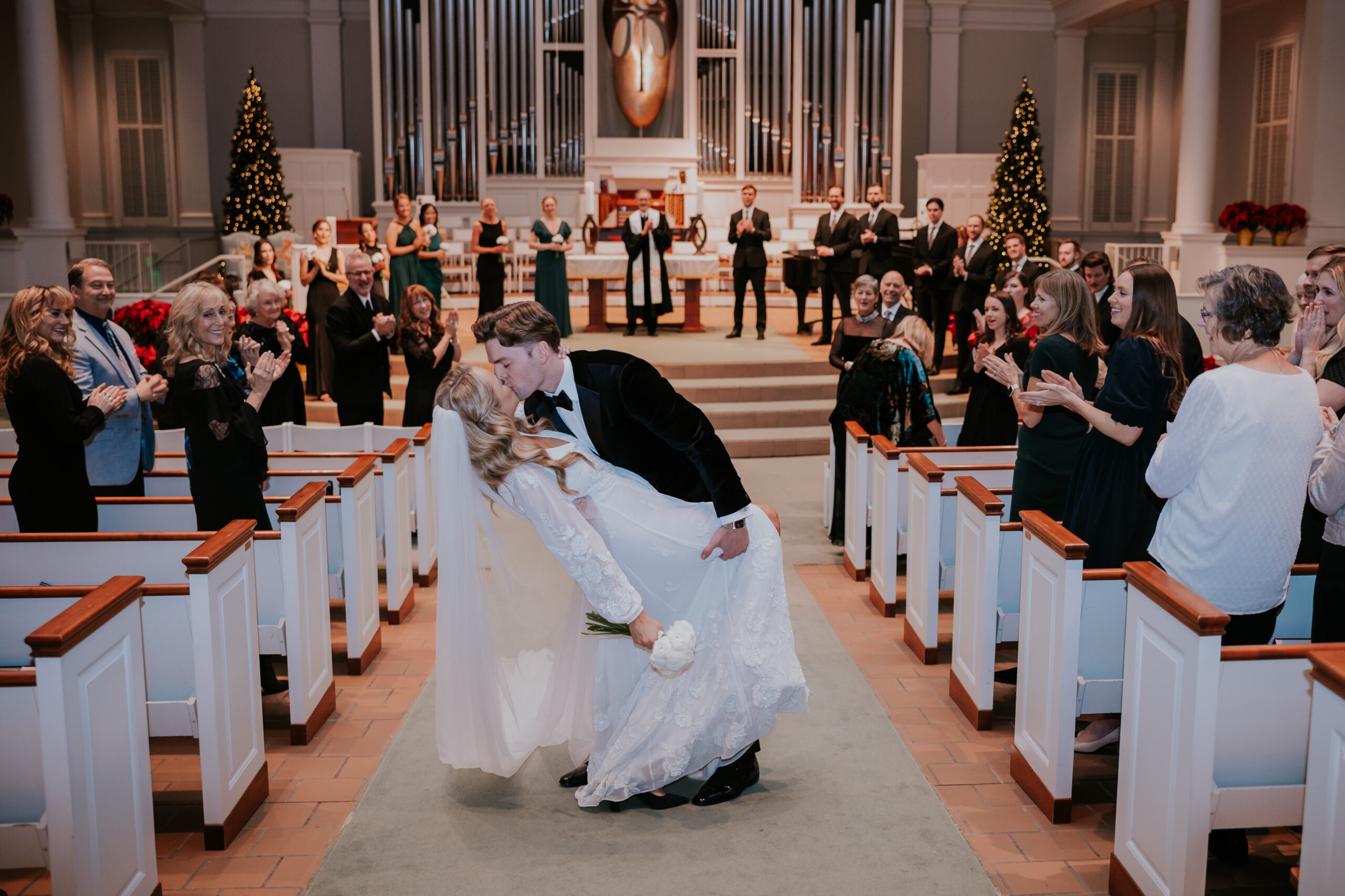 Bride and groom kissing at the end of the aisle as guests cheer, documented by a wedding photographer in Minnesota.