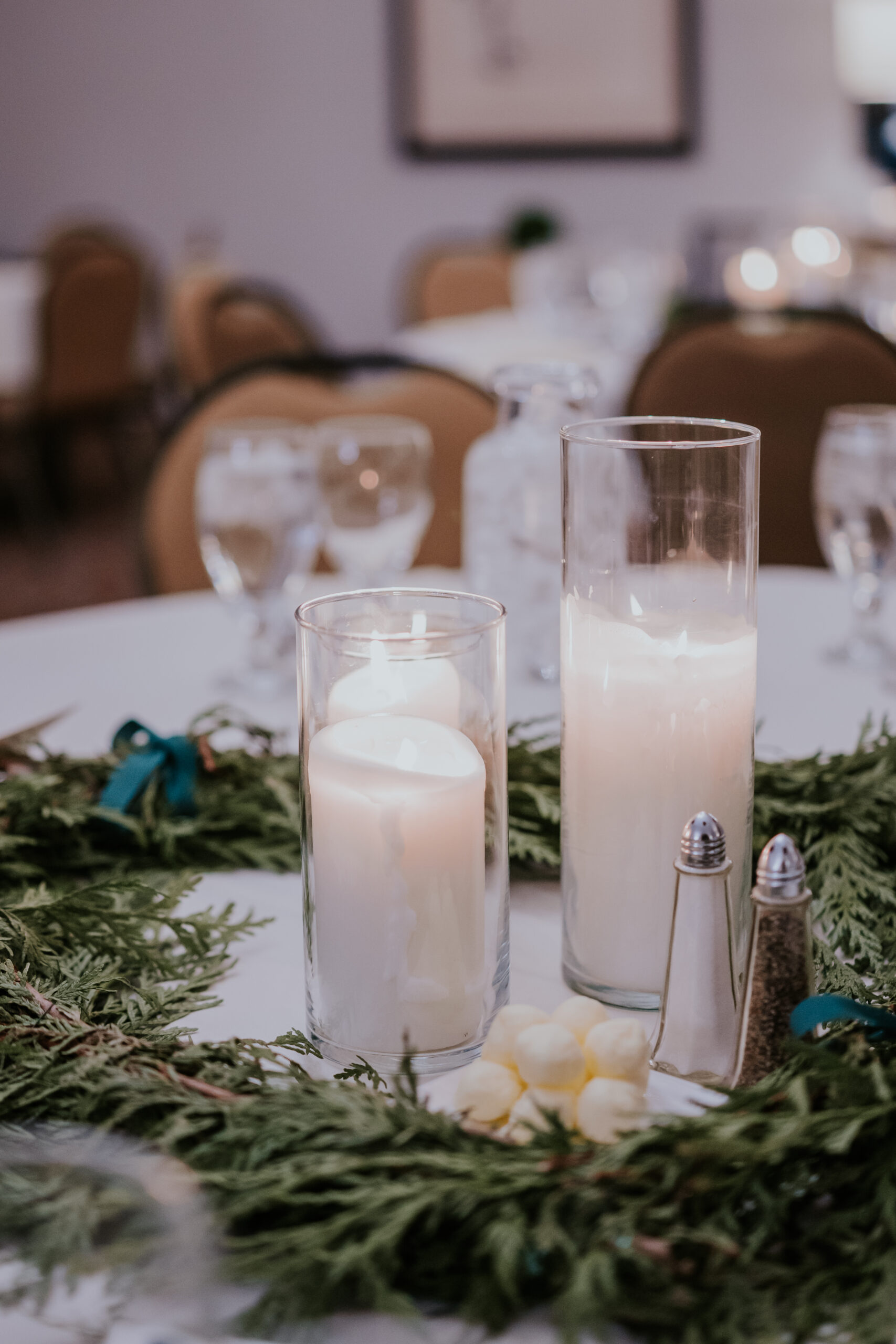 Candles in tall glass holders surrounded by greenery as part of the reception table centerpiece, photographed by a wedding photographer in Minnesota.