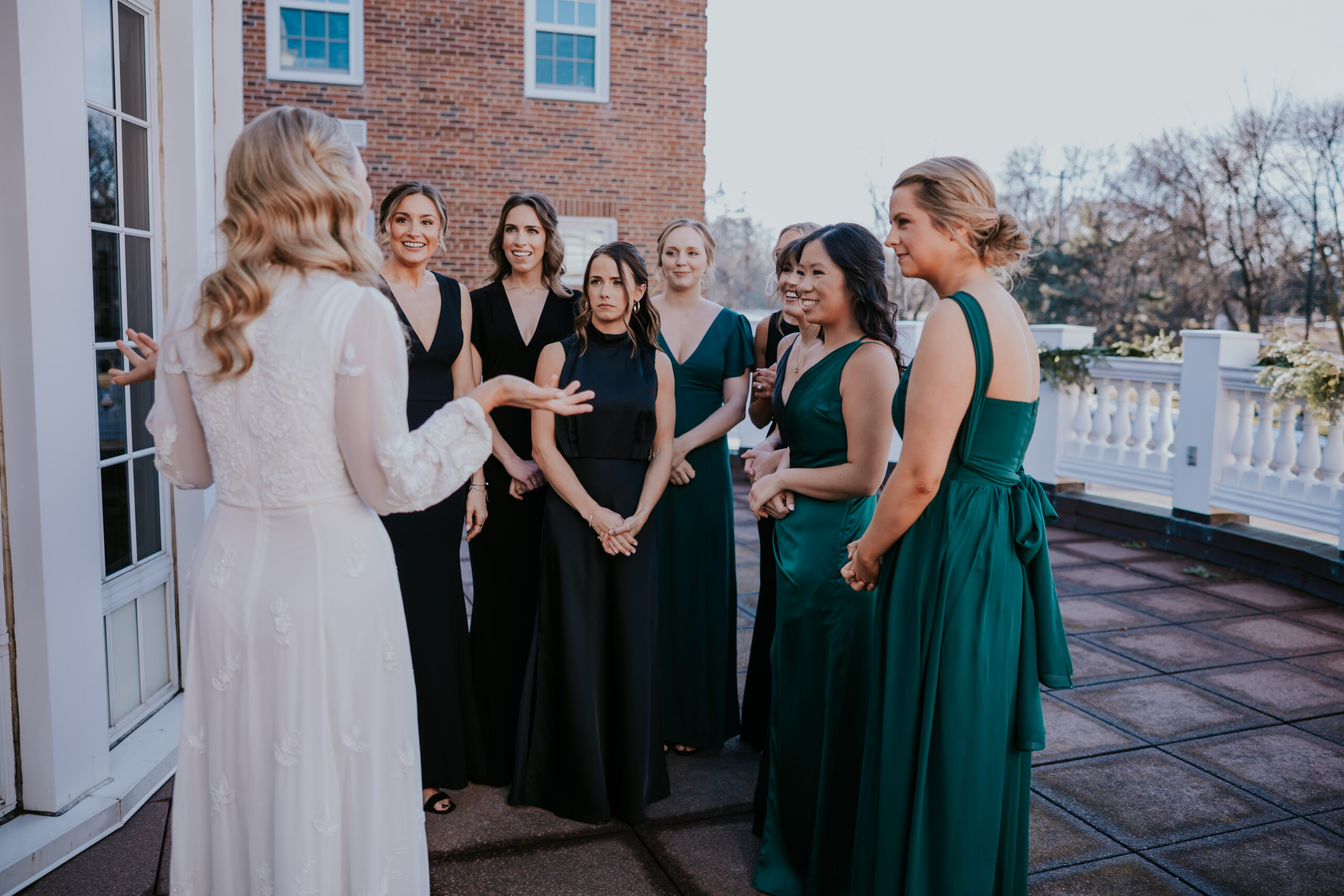 Bride showing her dress to bridesmaids wearing black and green gowns.