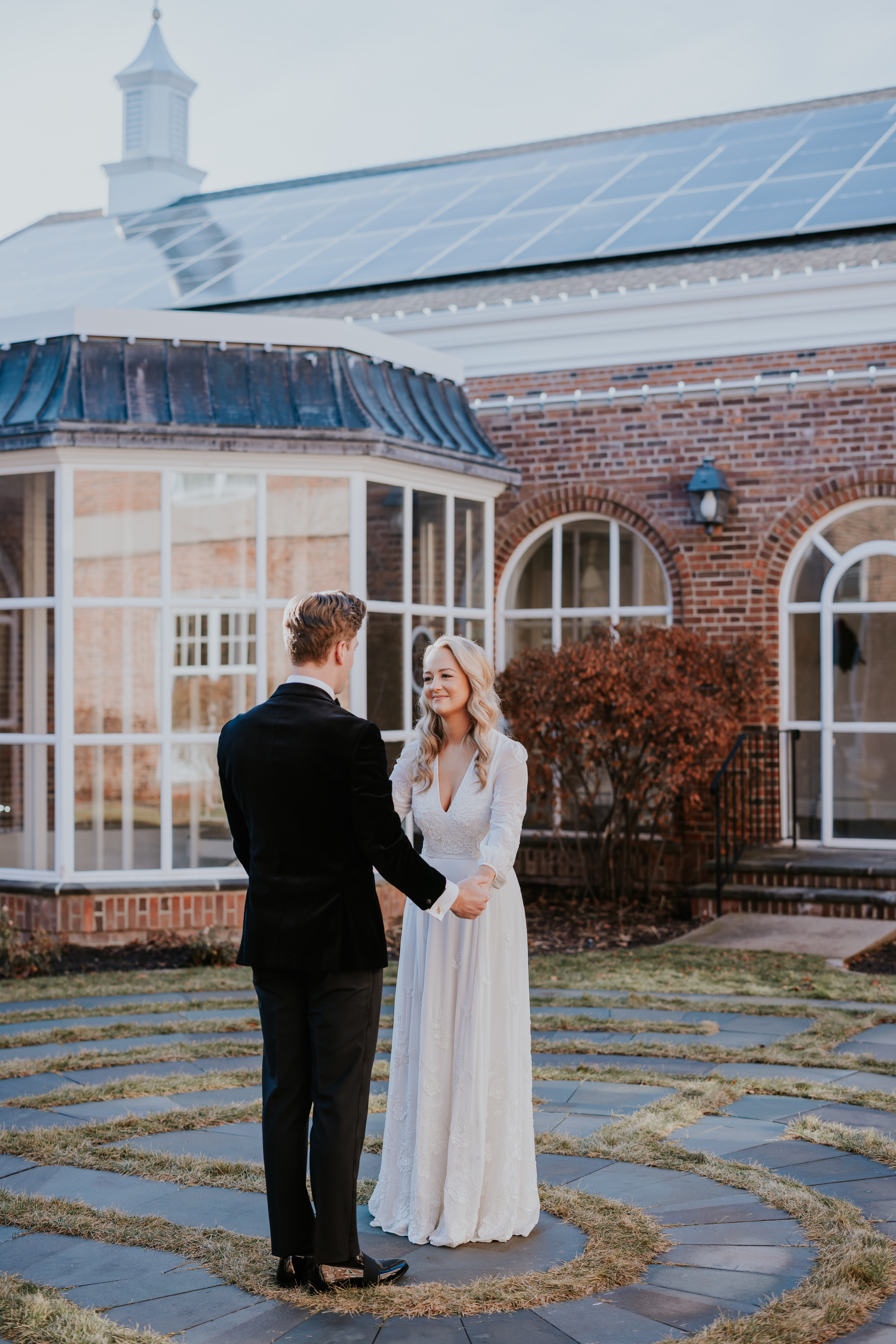 Groom holding the bride’s hand as they smile at each other outdoors.