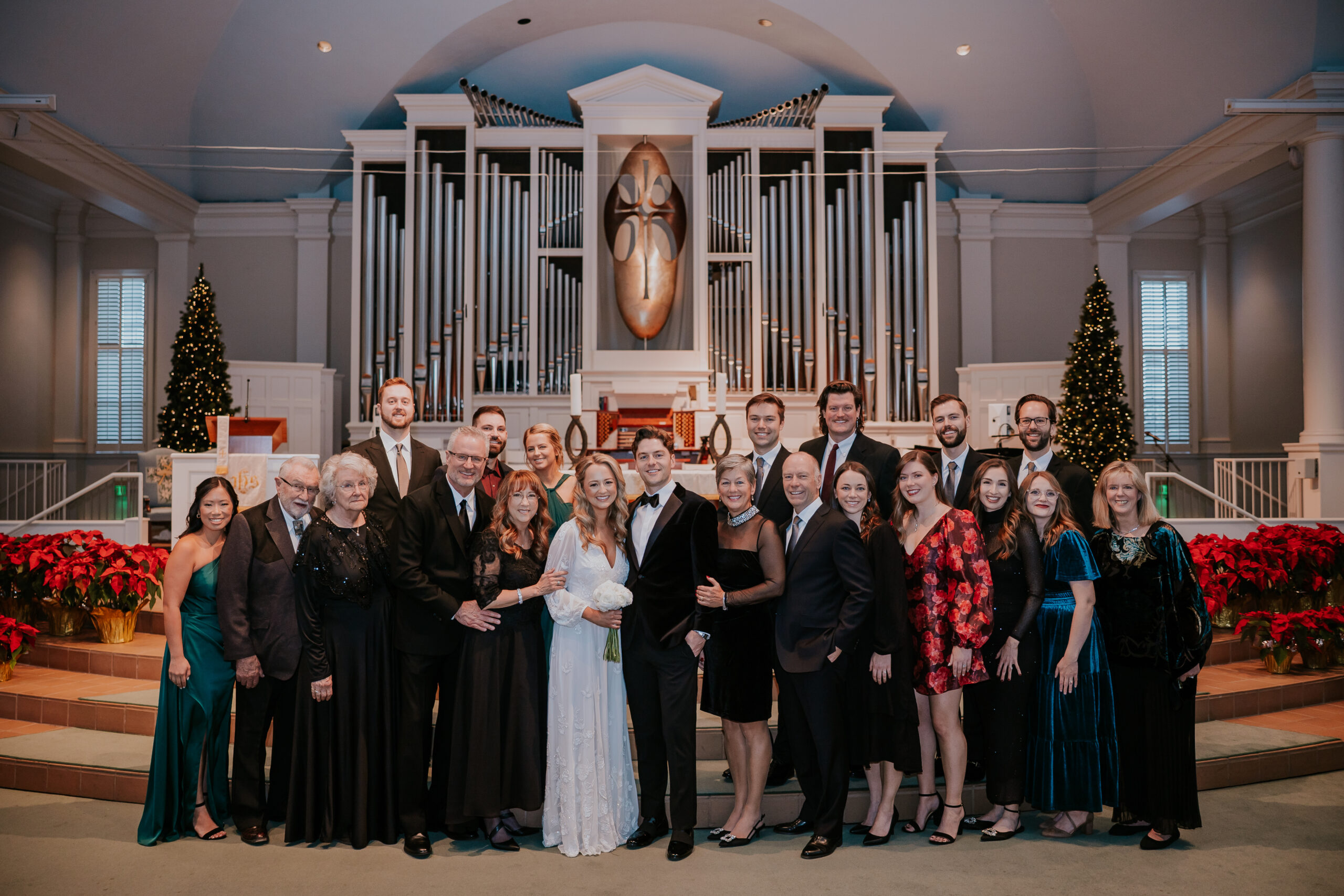 Large family group gathered around the bride and groom inside a church with grand organ pipes.