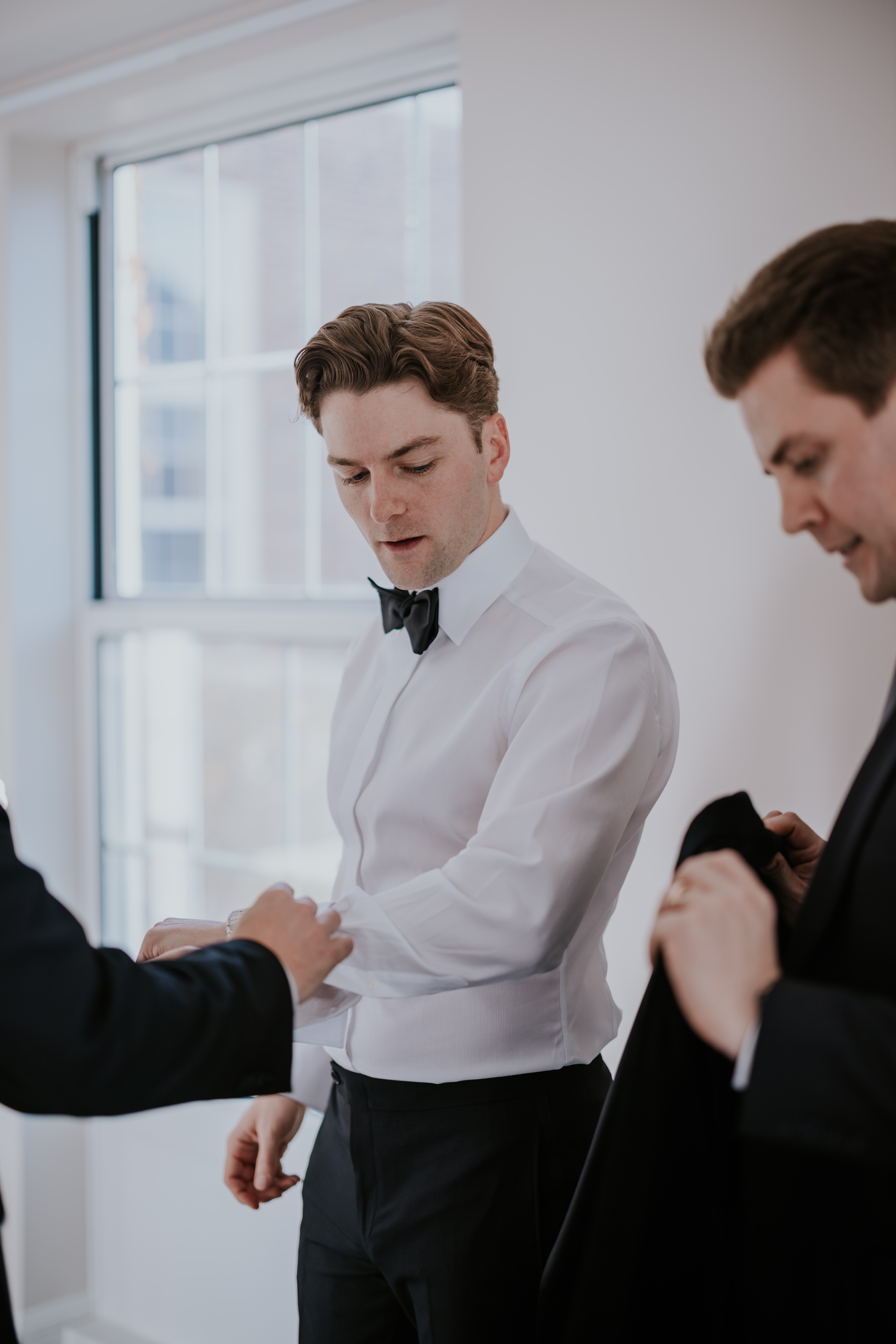 Groom adjusting his cufflinks while preparing for the wedding with his groomsmen.