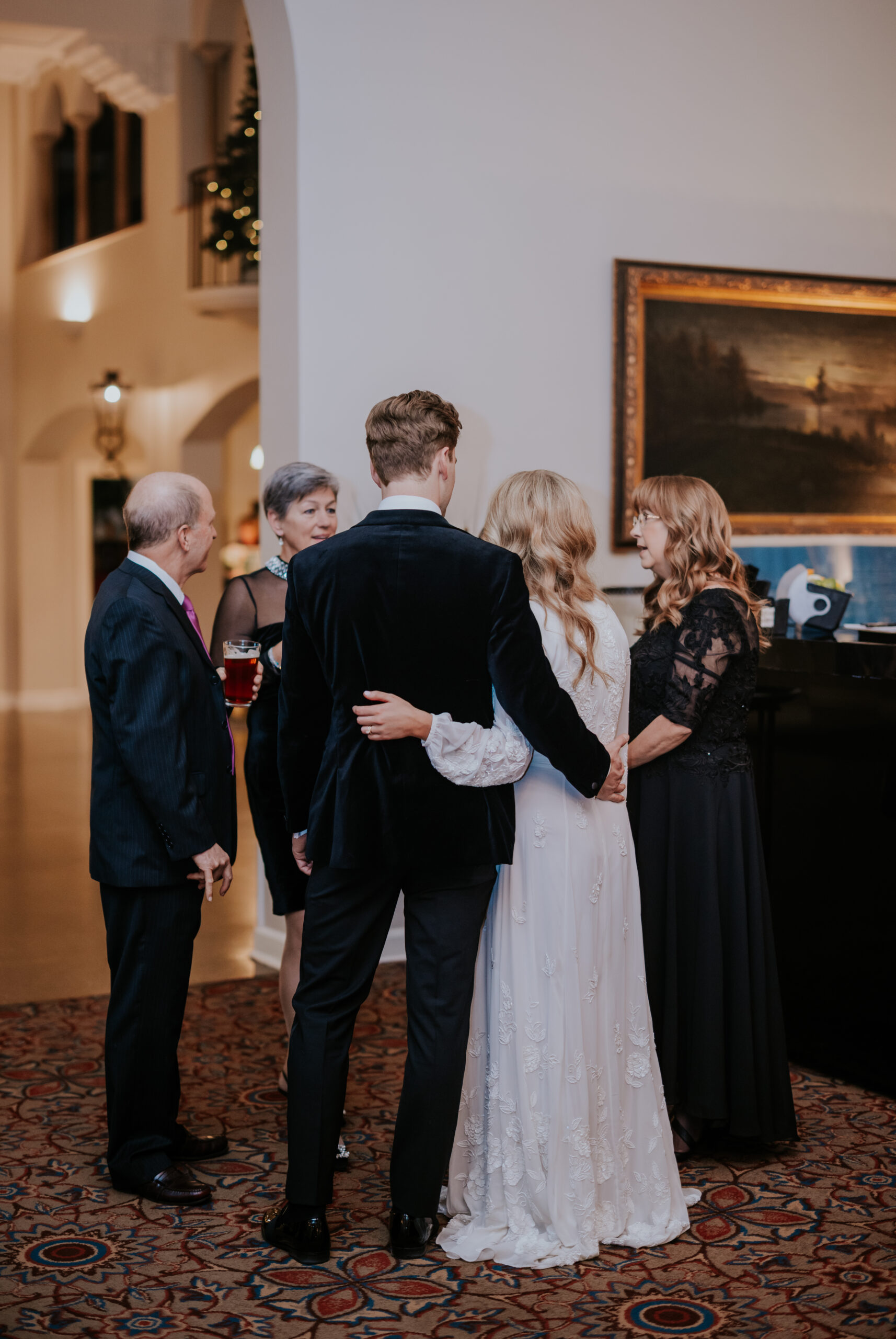 Bride and groom standing with arms around each other while chatting with family members during the reception.