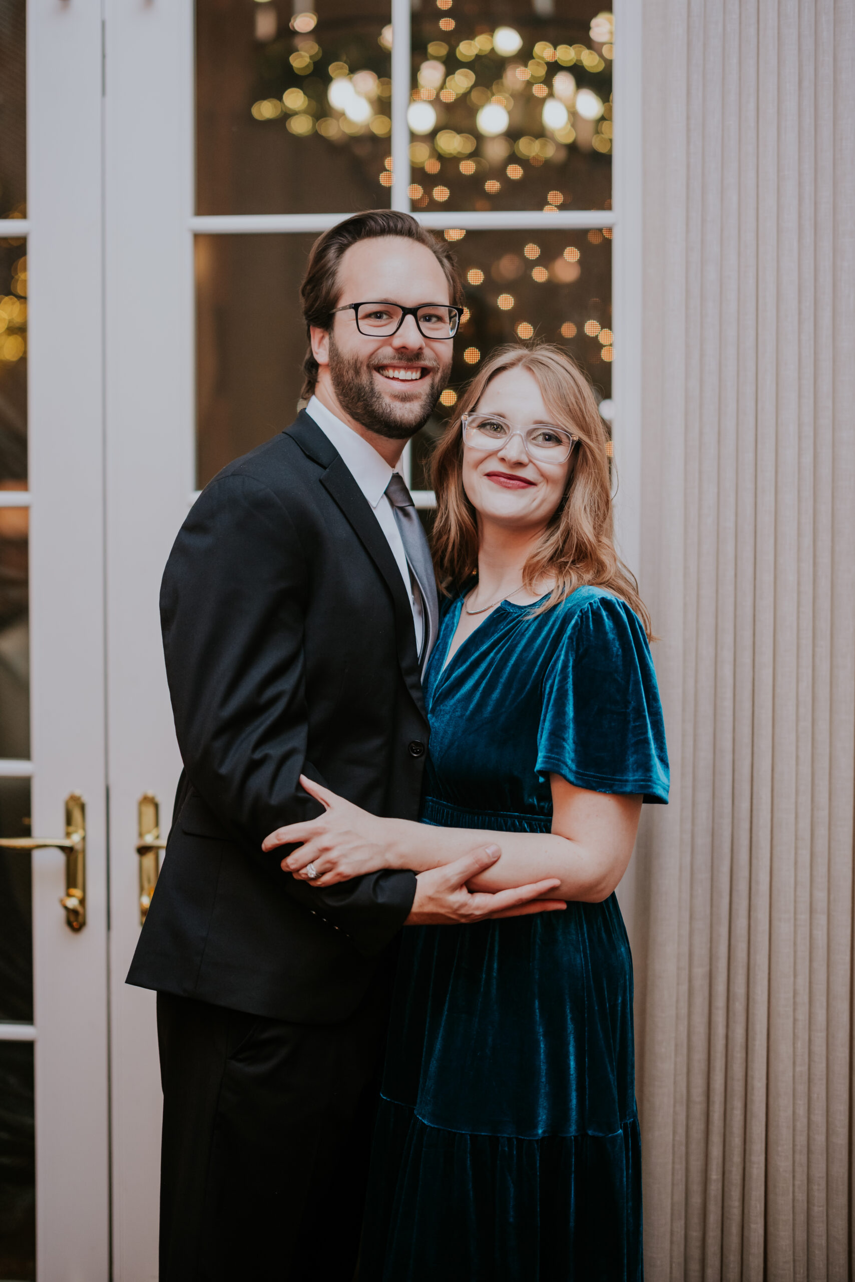 Smiling couple posing together, the woman in a teal velvet dress and the man in a suit, photographed by a wedding photographer in Minnesota.