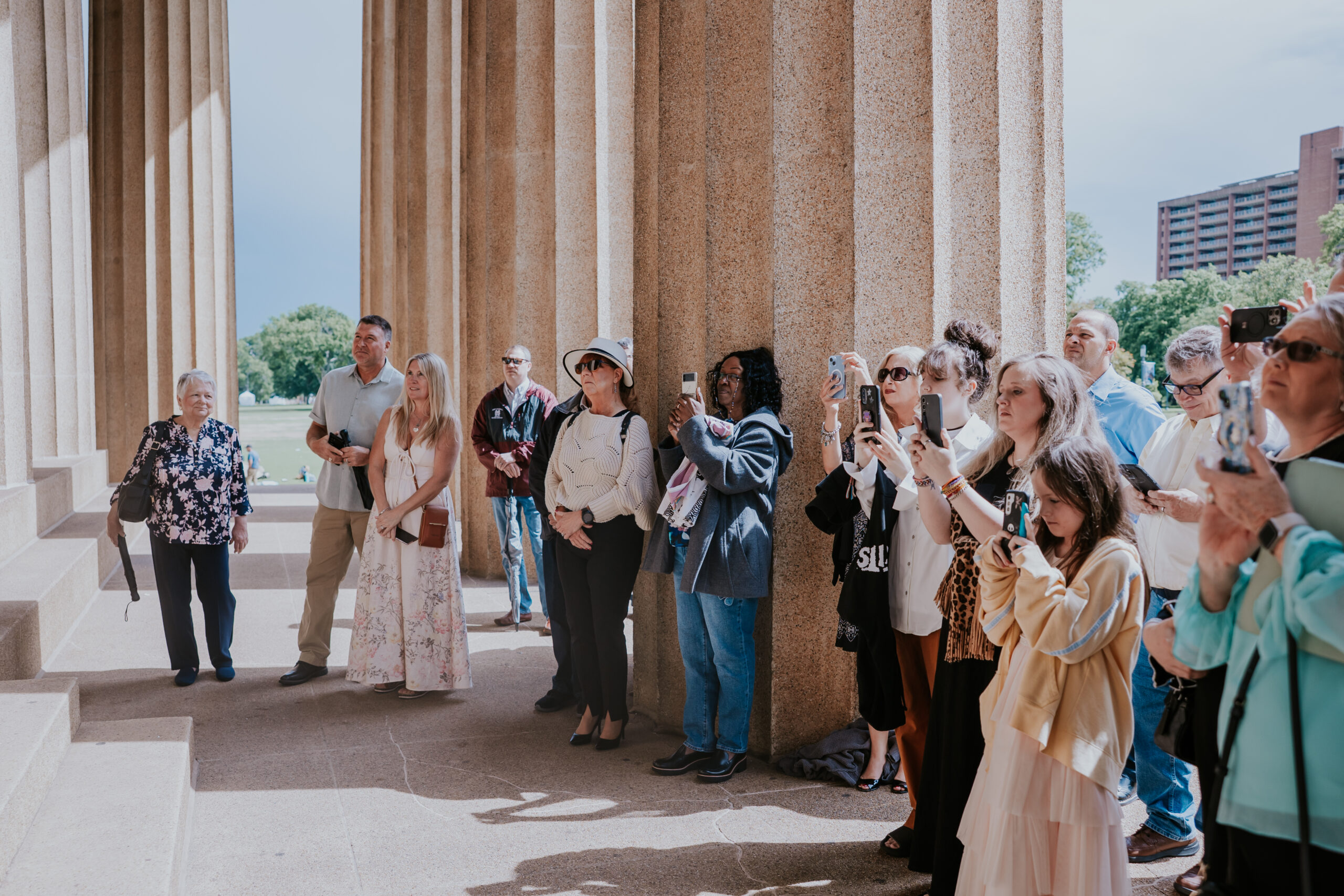 Guests gathered at a wedding ceremony under grand stone columns, all taking photos of the couple.