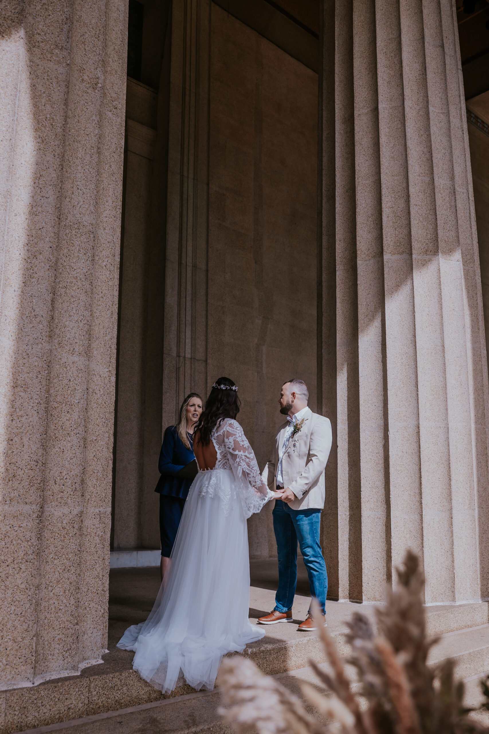 Wide angle view of bride and groom exchanging vows beneath towering architecture in a romantic travel wedding setting.