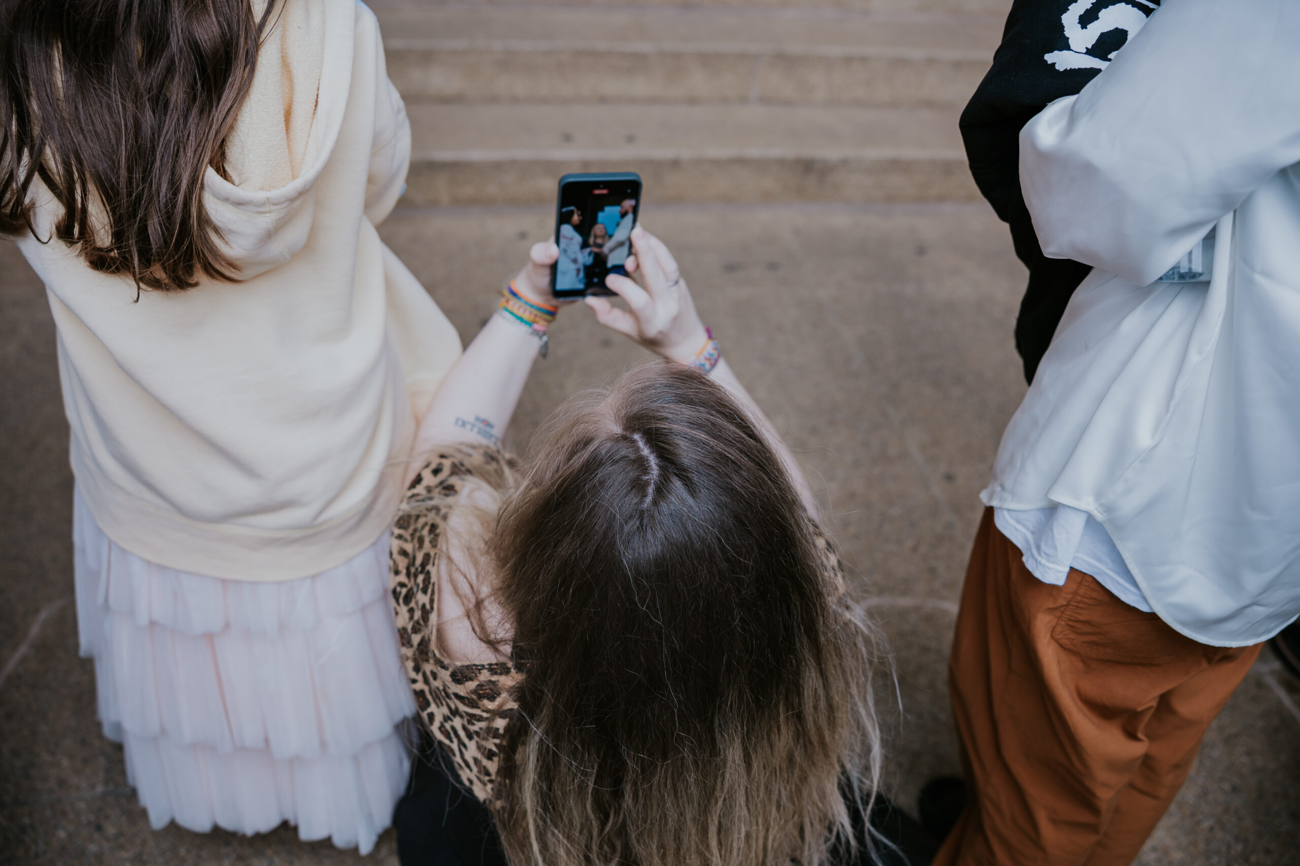 Woman kneeling to capture wedding photos on her phone during an outdoor ceremony.