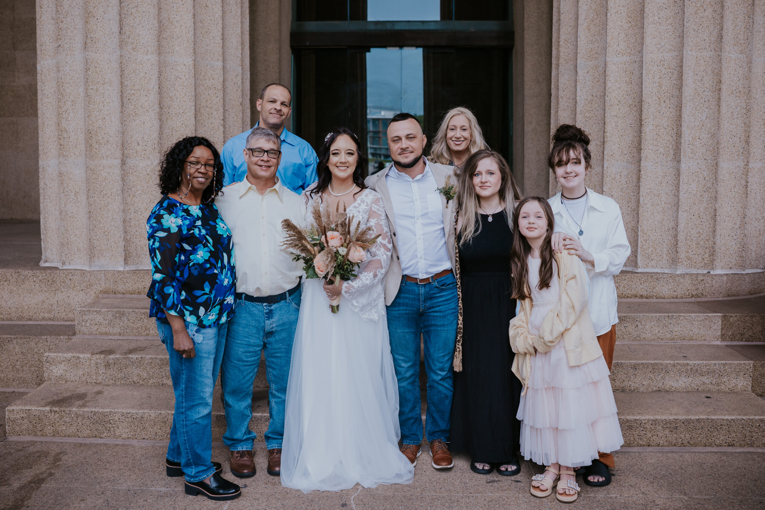 Bride and groom pose with loved ones on wedding day steps, a heartfelt moment preserved by a travel wedding photographer.