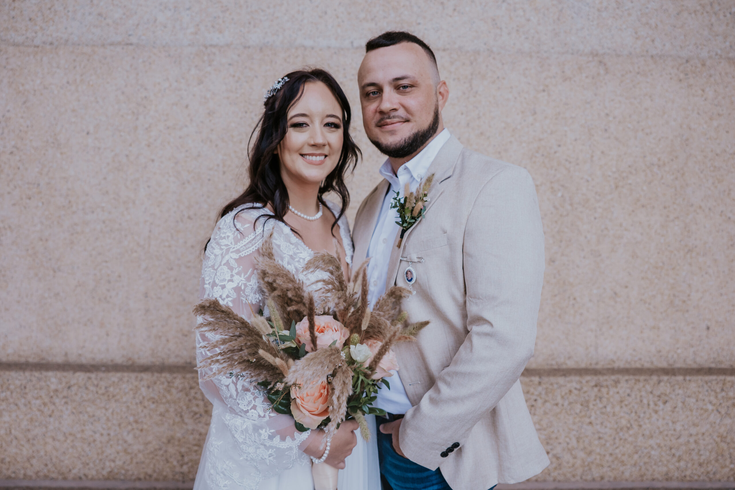 Couple smiling at the camera in a relaxed wedding portrait, with bride holding bouquet and groom wearing jeans—perfectly captured by a travel wedding photographer.