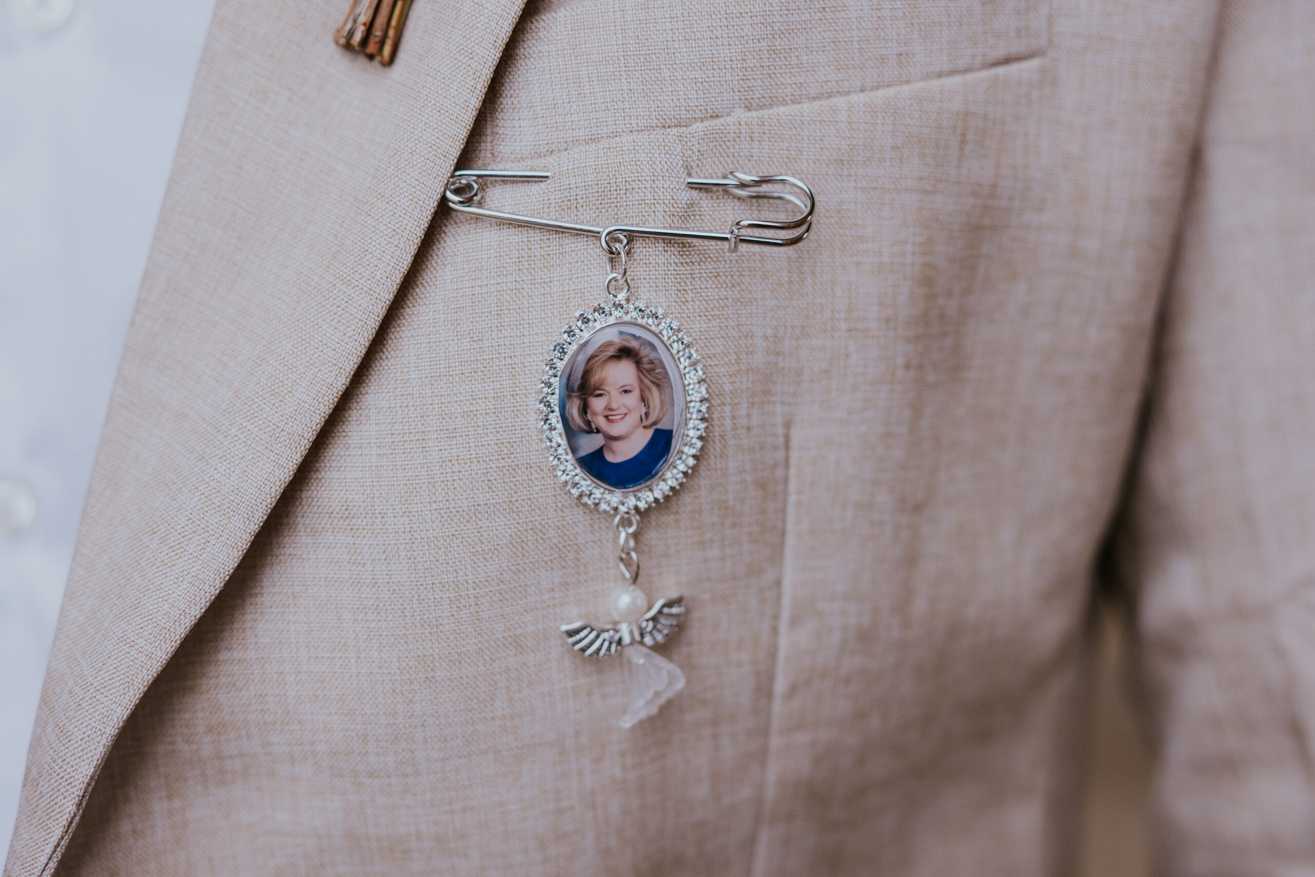 Memorial pin with photo and angel charm fastened to groom’s jacket lapel, honoring a loved one on wedding day.