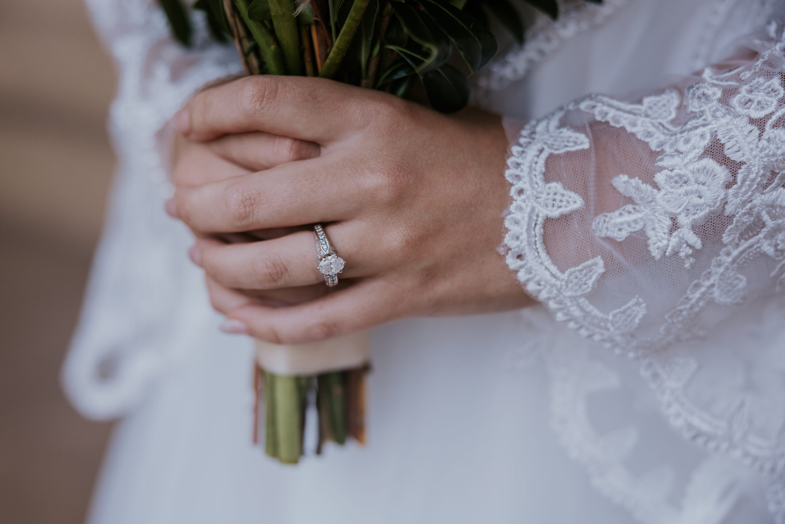 Close-up of bride's hands holding her bouquet, showing off her diamond engagement ring and lace bell sleeves.