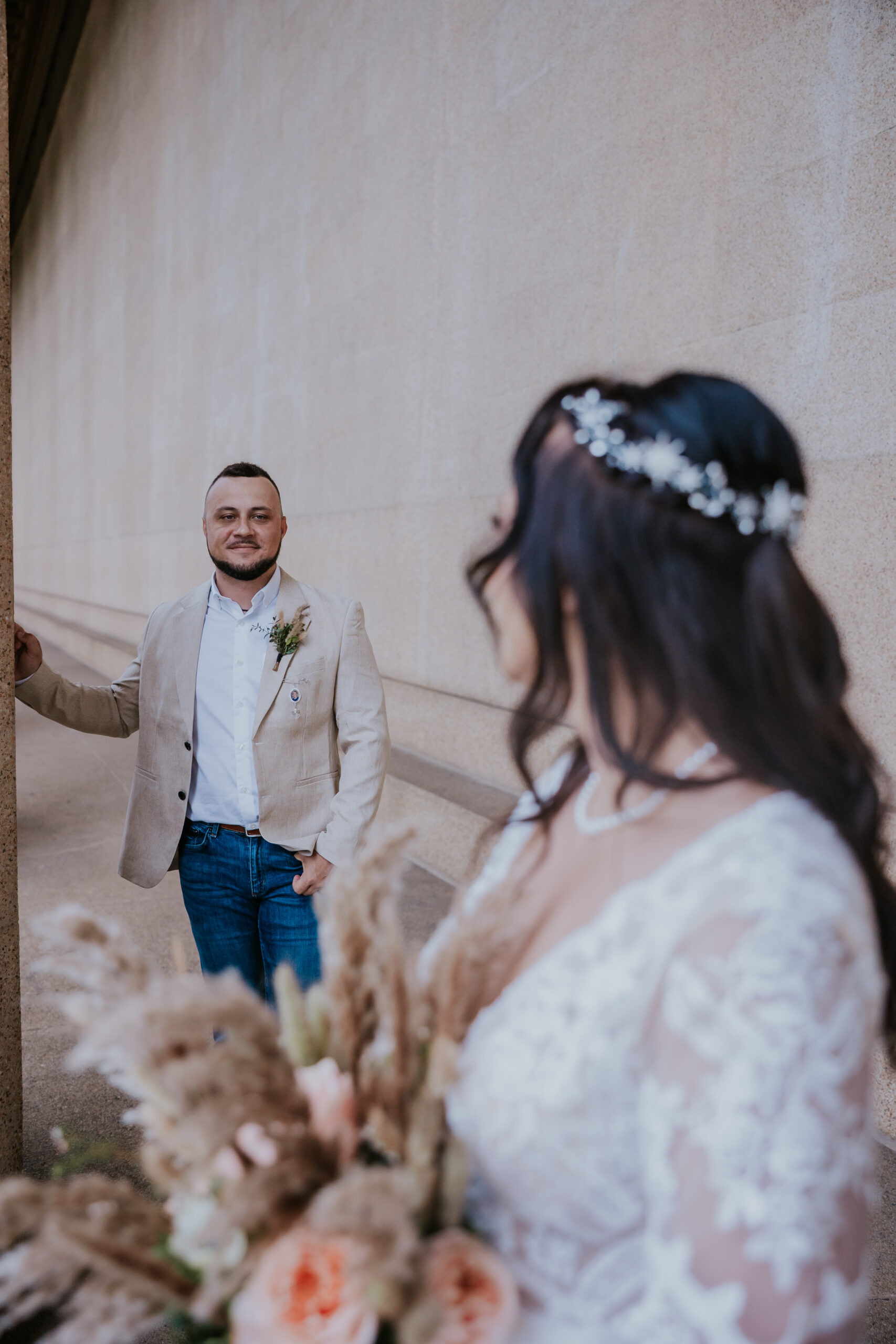 Groom smiles at his bride during a romantic first look, captured by a travel wedding photographer in an elegant architectural setting.