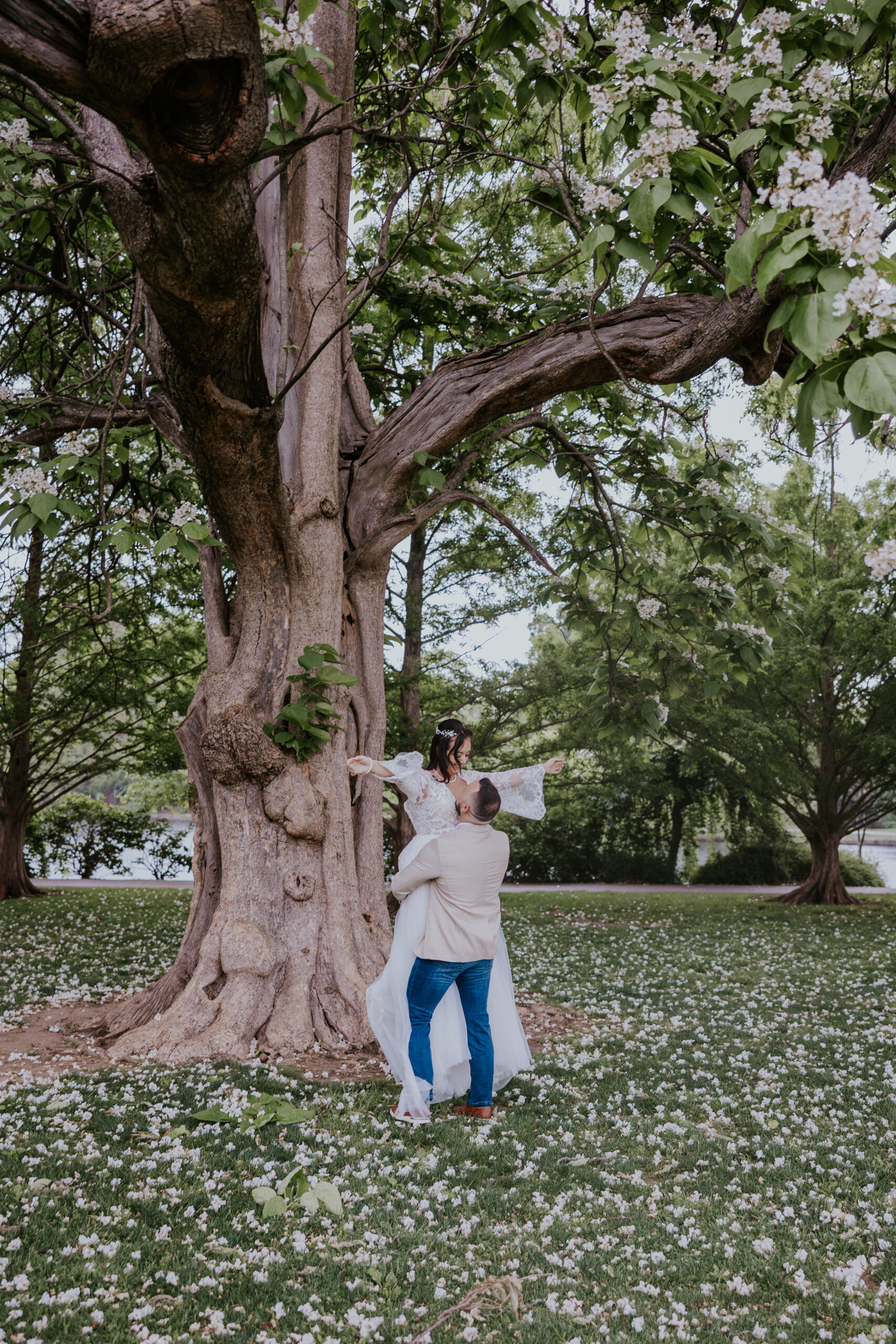 Under a canopy of spring blossoms, the groom lifts his bride in celebration—an unforgettable capture by a travel wedding photographer.