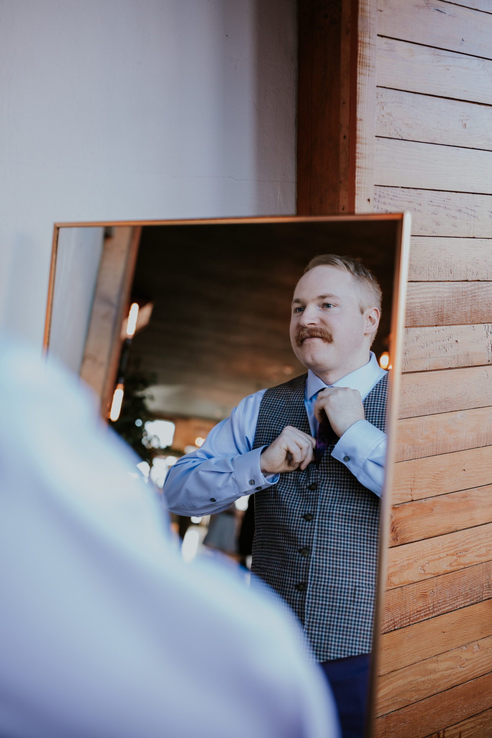 Groom adjusting his tie in front of a mirror, finishing touches before walking down the aisle.