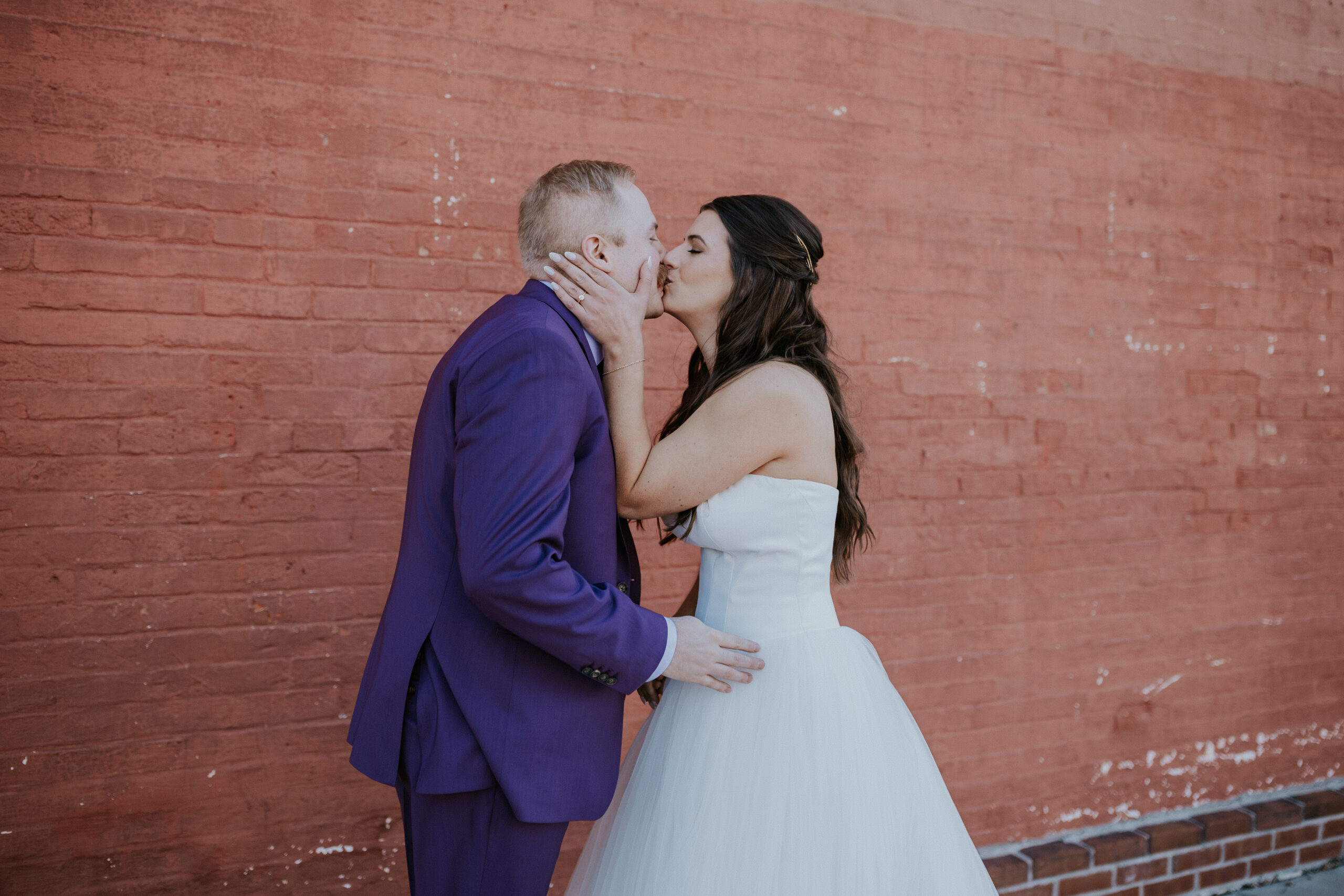 Bride and groom sharing a kiss in front of a red brick wall during their first look.