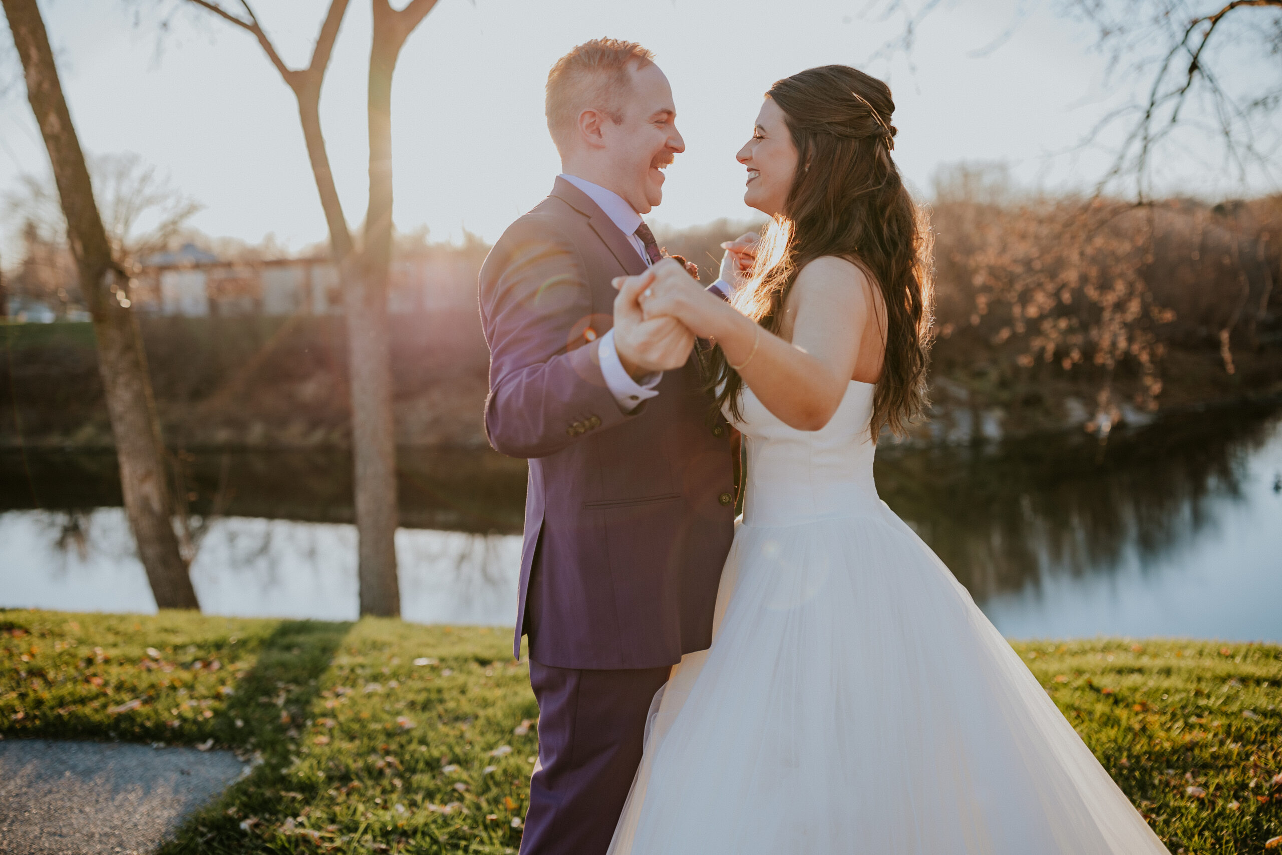 Couple dancing outdoors, holding hands and smiling at each other as the sun sets behind them.