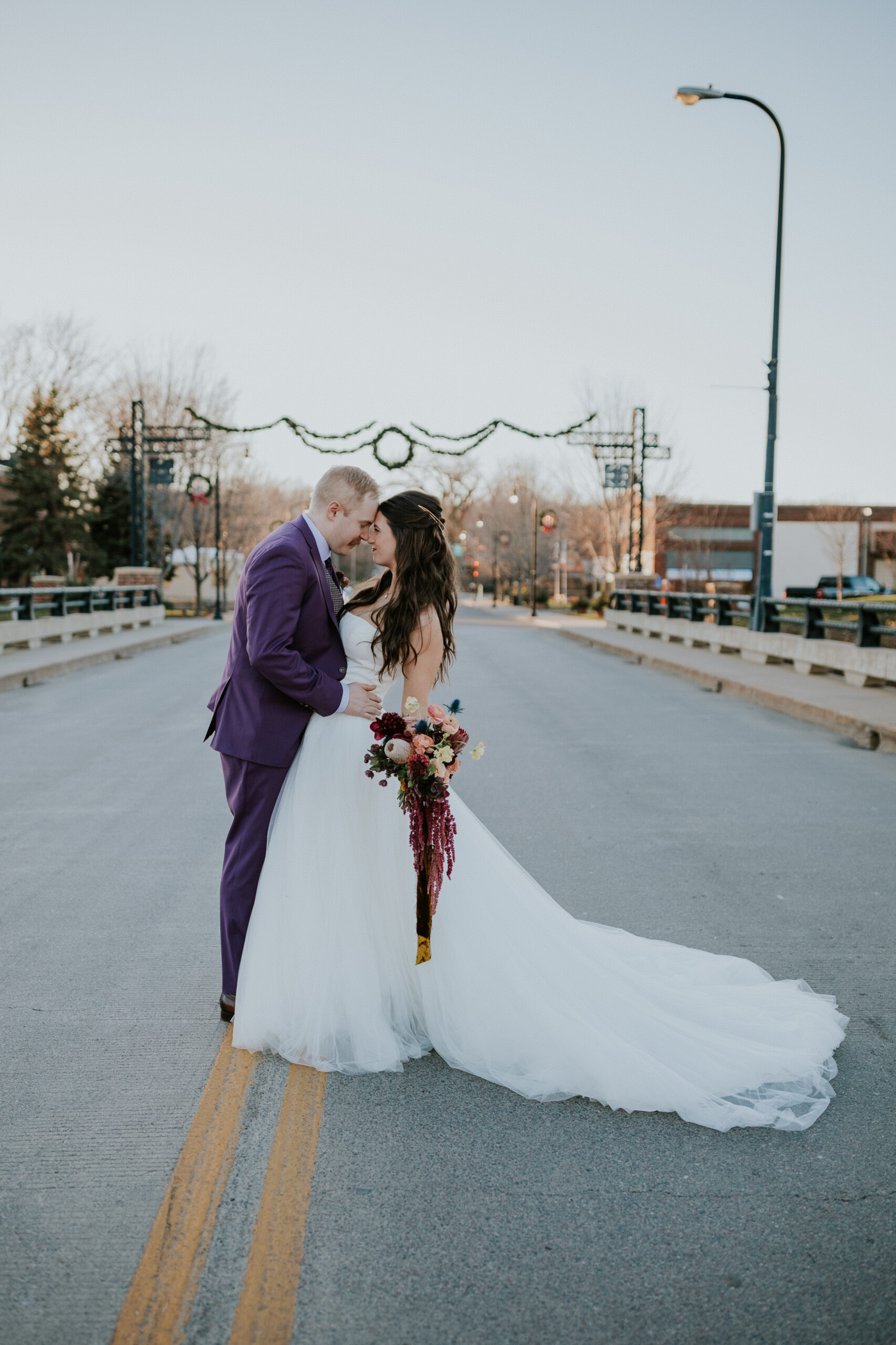 Bride and groom kiss in the middle of a quiet downtown street, holding a bouquet of rich fall flowers—captured by destination wedding photographers.