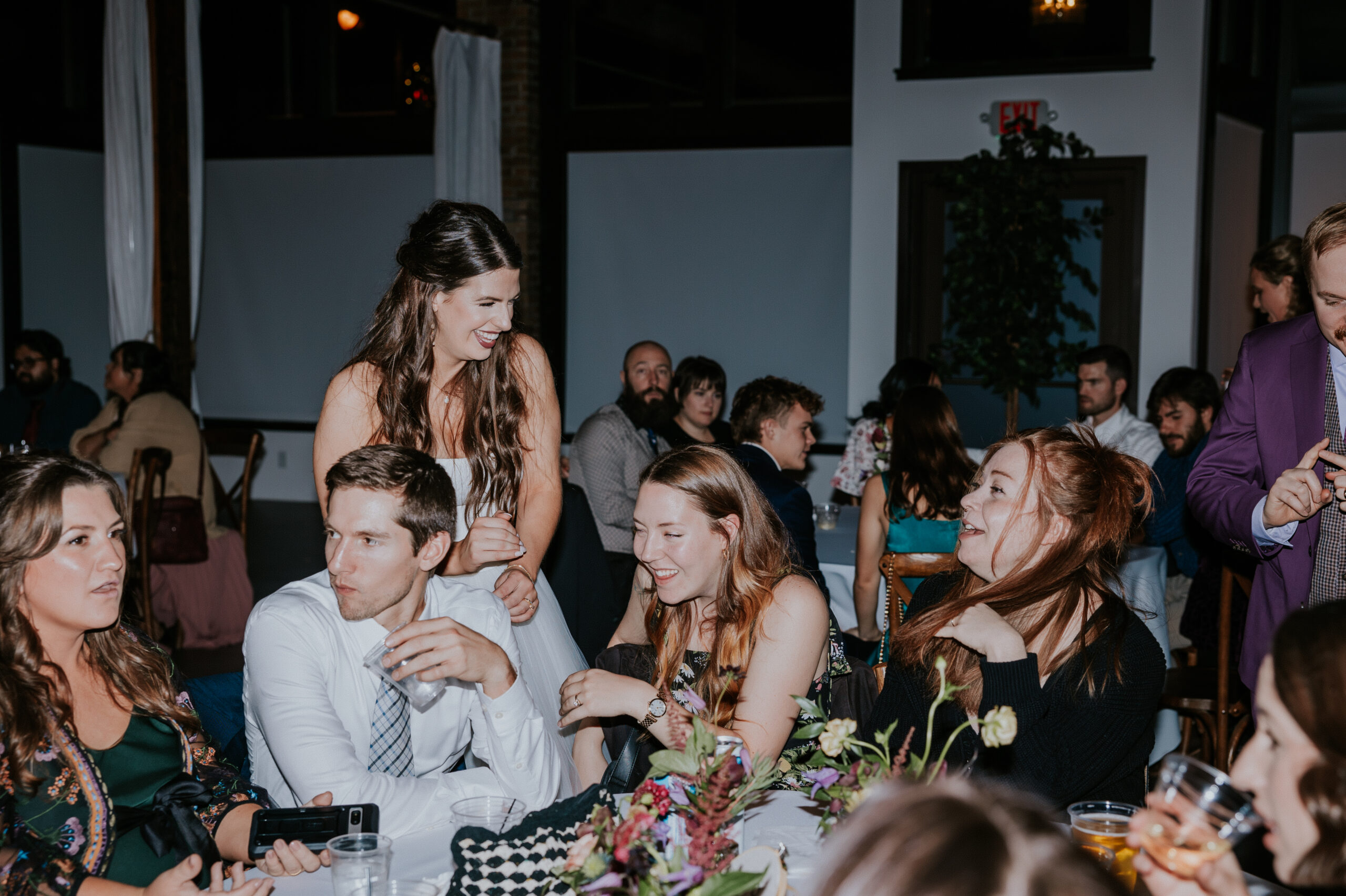 Bride leaning over to talk with guests at a reception table, full of laughter and connection—ideal for destination wedding photographers.