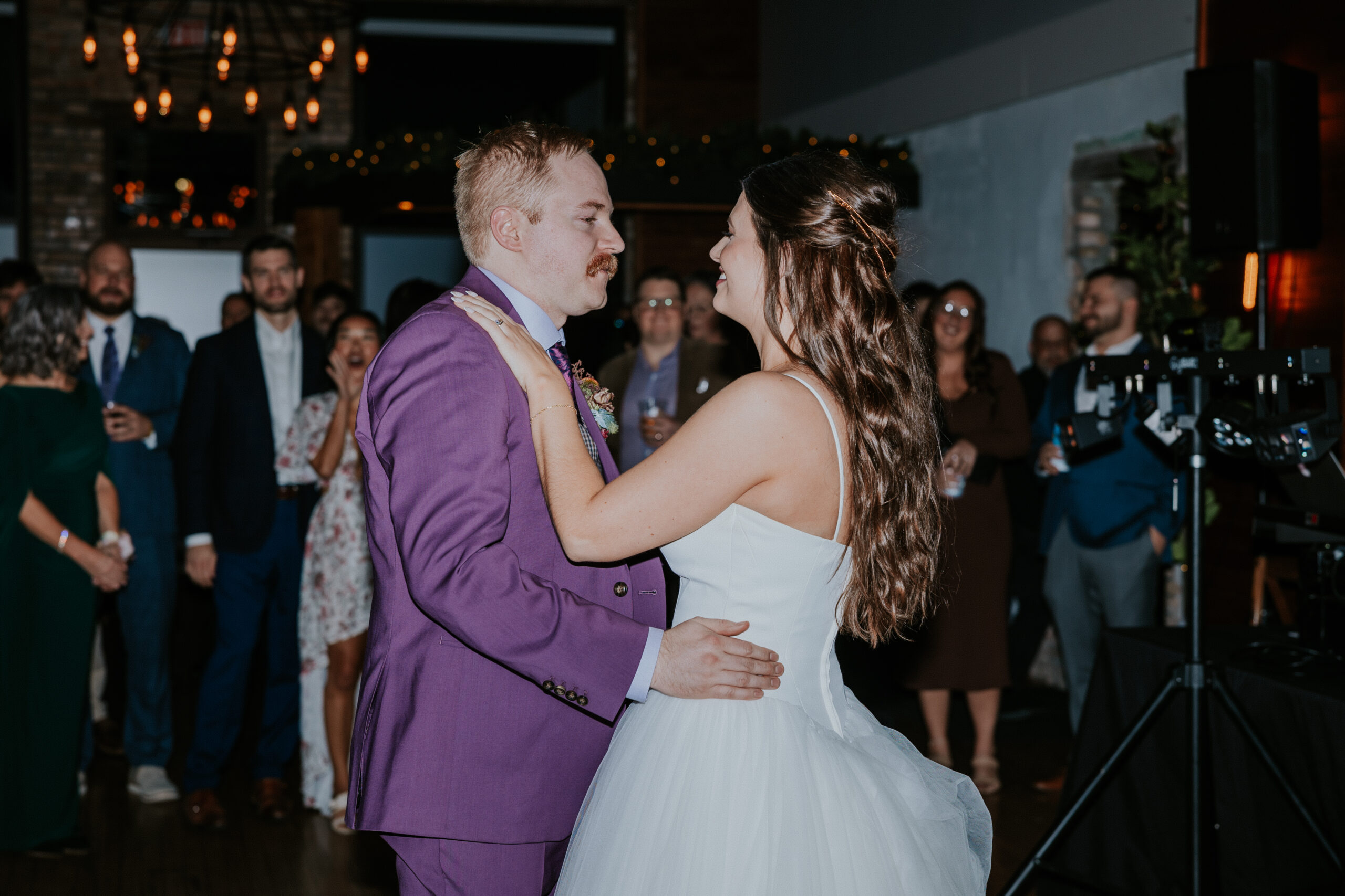 First dance moment between bride and groom, with family and friends looking on.