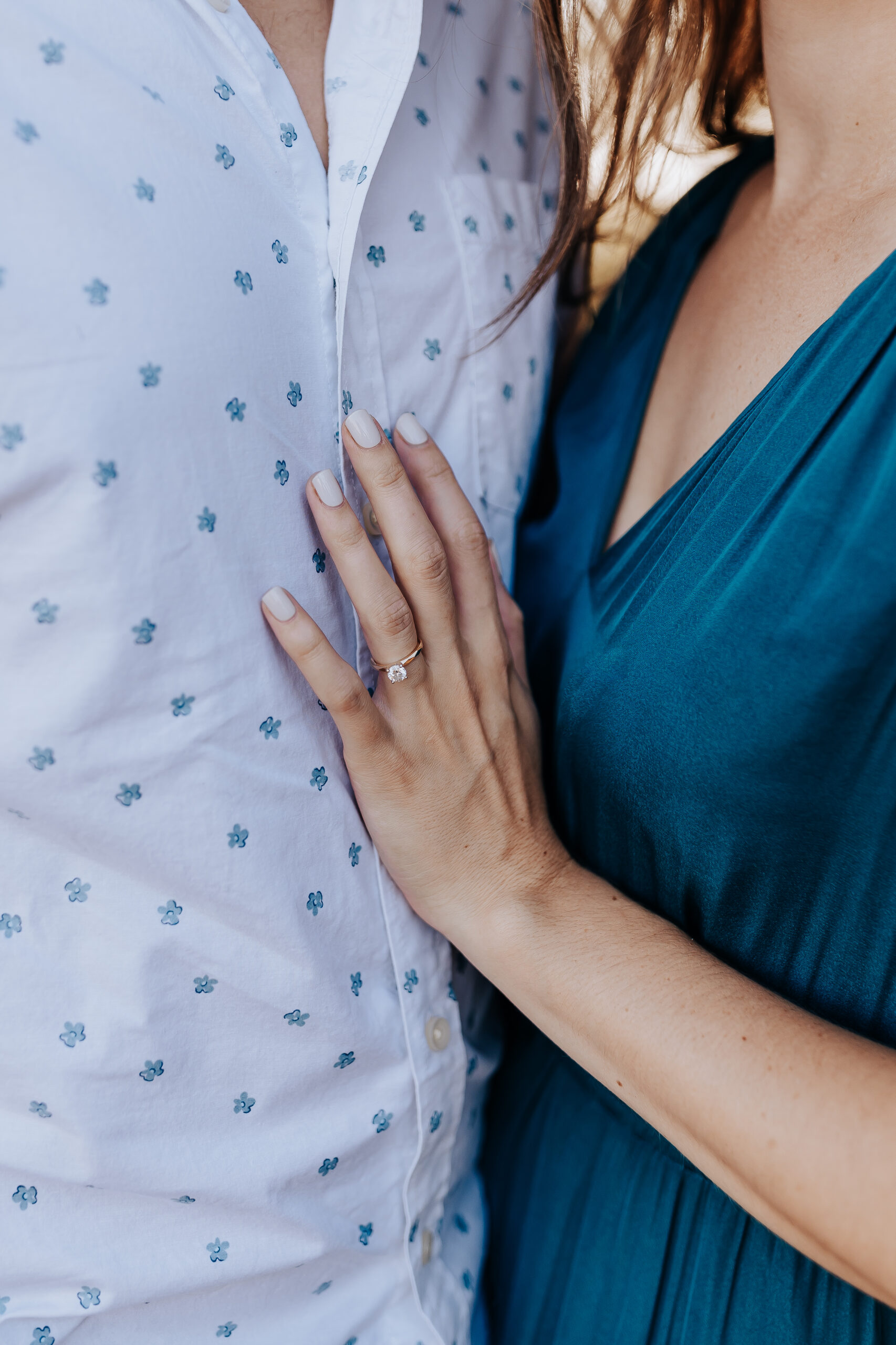 Close-up of a bride-to-be resting her hand on her partner’s chest, showing off her delicate engagement ring.