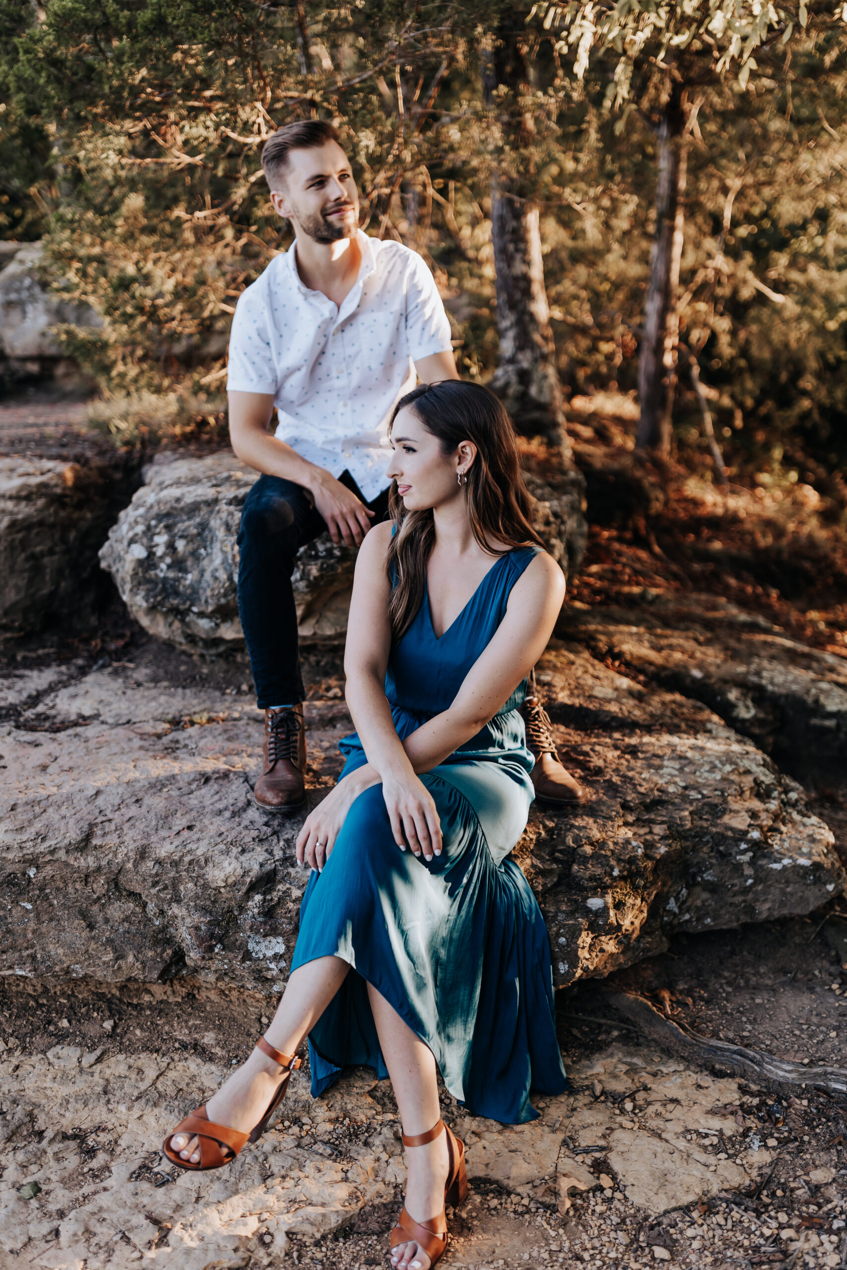 A man and woman sit on a sunlit rock, sharing a quiet moment during their nature-filled engagement session.