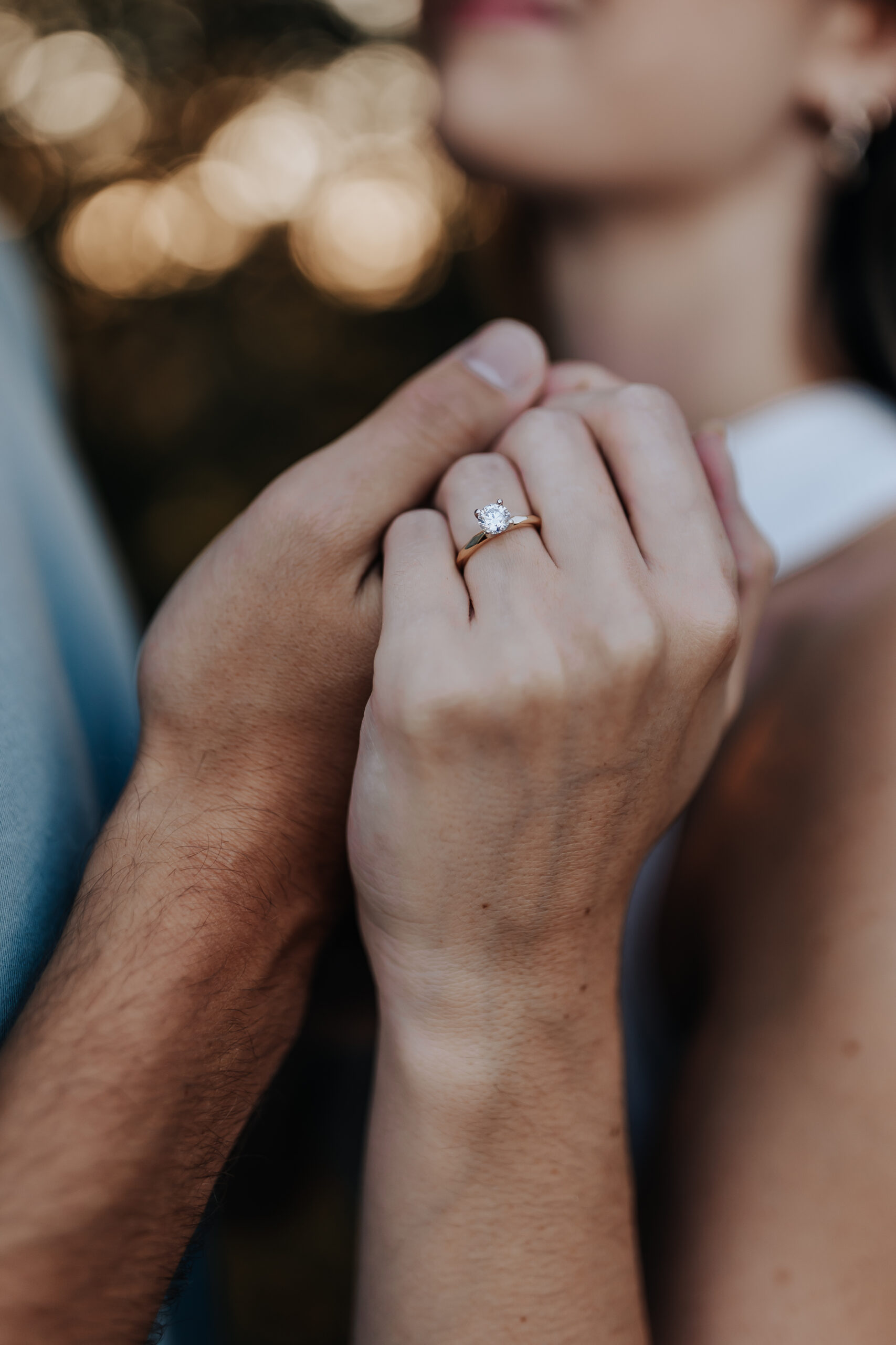 Close-up of the bride-to-be’s hand showing off her engagement ring as she holds her partner’s hand gently.