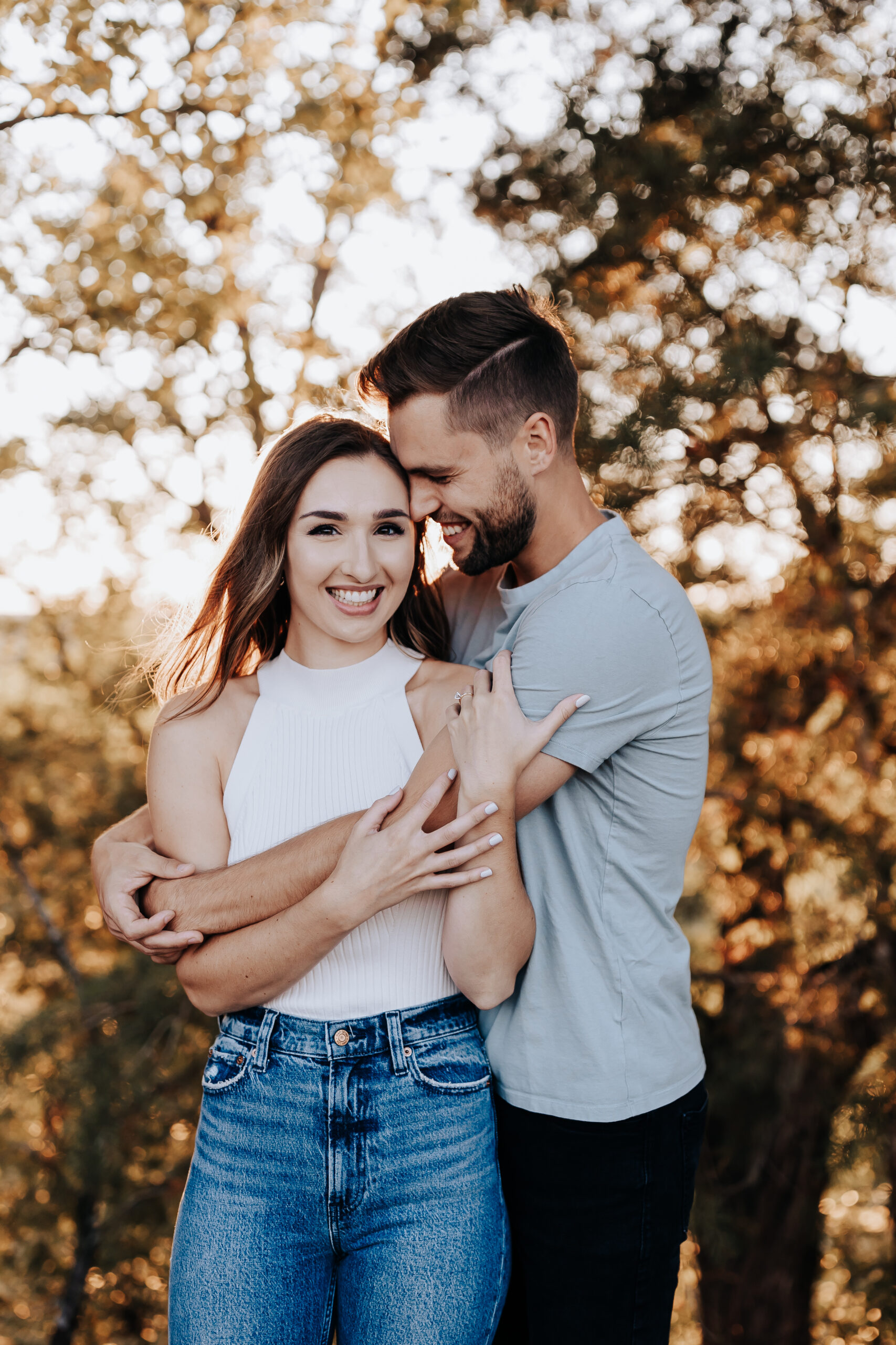 A sweet embrace between a smiling bride-to-be and her fiancé, framed by golden forest light, captured by a Nashville engagement photographer.