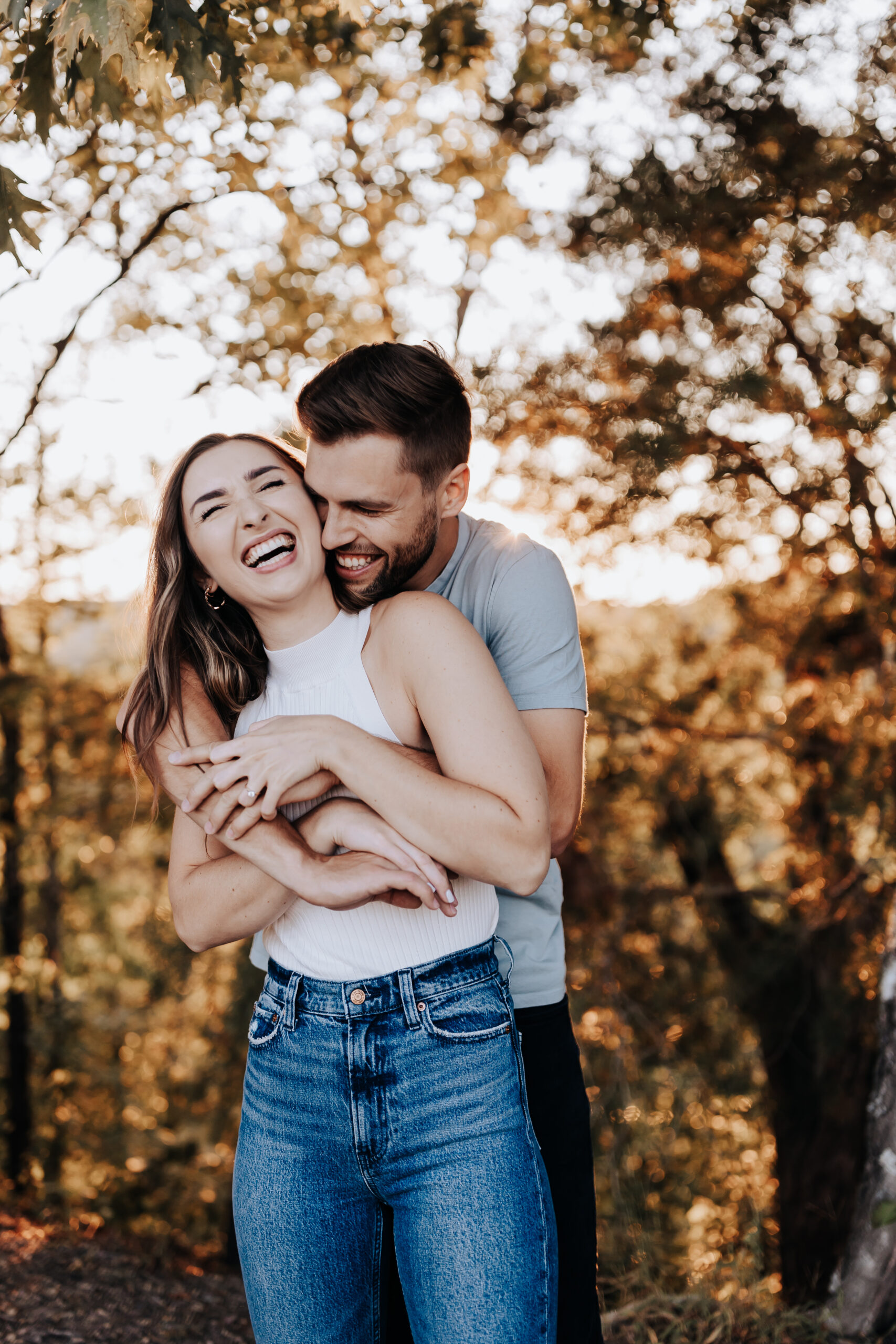 A candid, joyful hug from behind as a woman laughs with her partner in the woods during a golden-hour session with a Nashville engagement photographer.