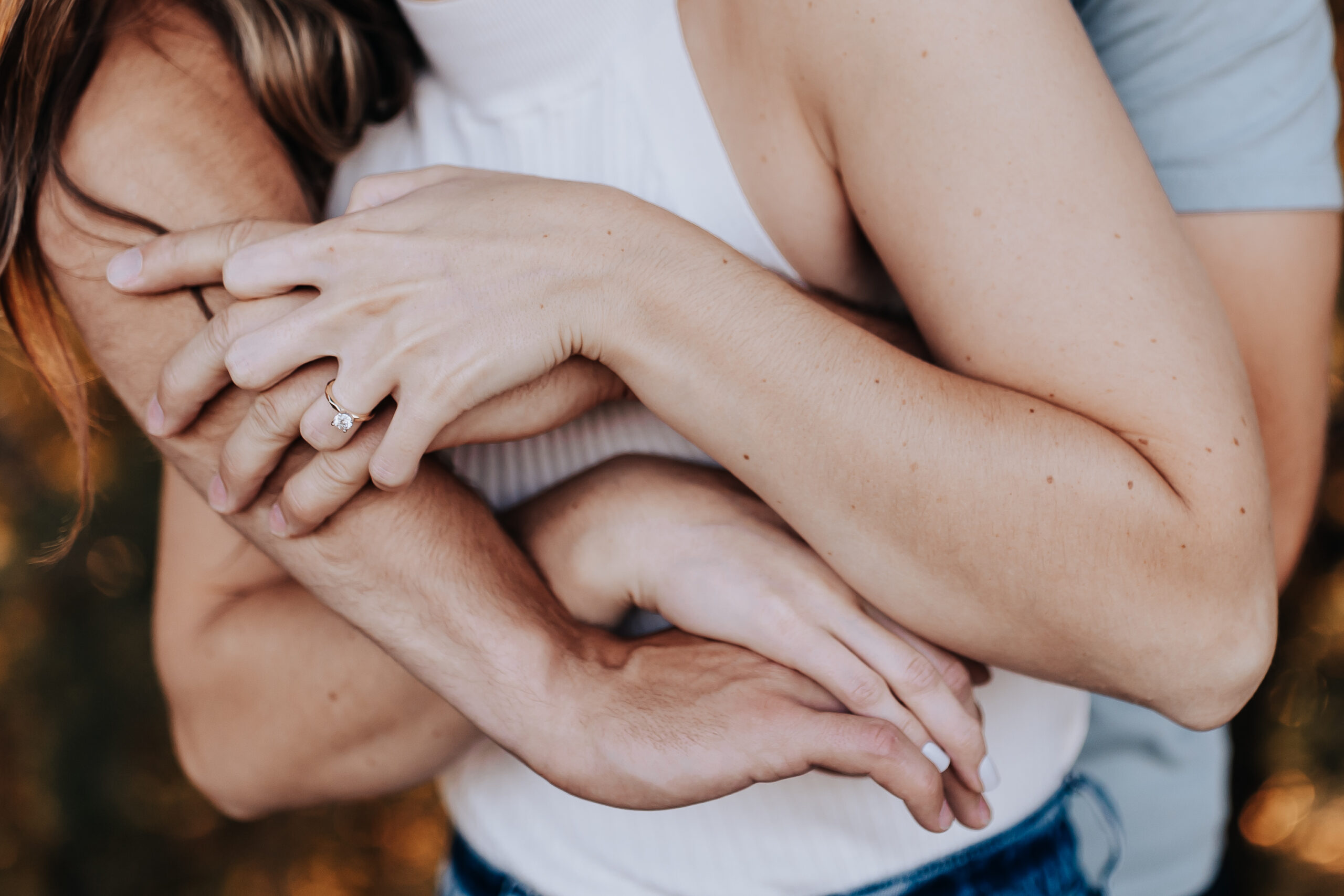 Close-up of intertwined arms, showing an engagement ring as the couple embraces during their Nashville engagement photographer session.