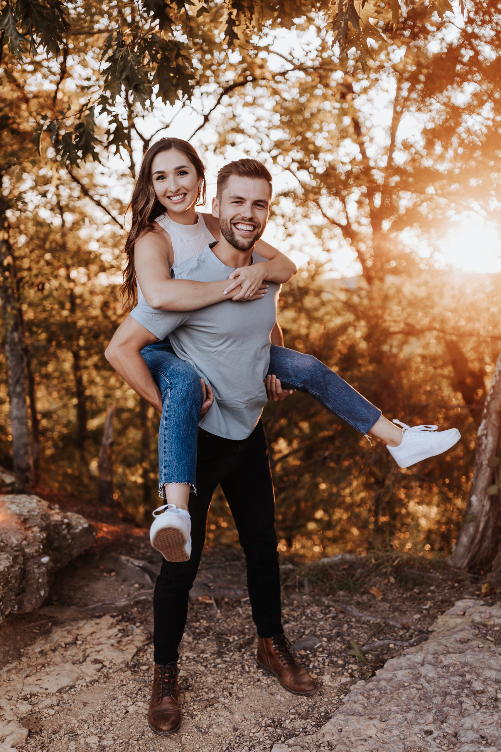 A playful piggyback ride through the woods as the sun sets behind the couple, laughter and joy radiating from the moment.