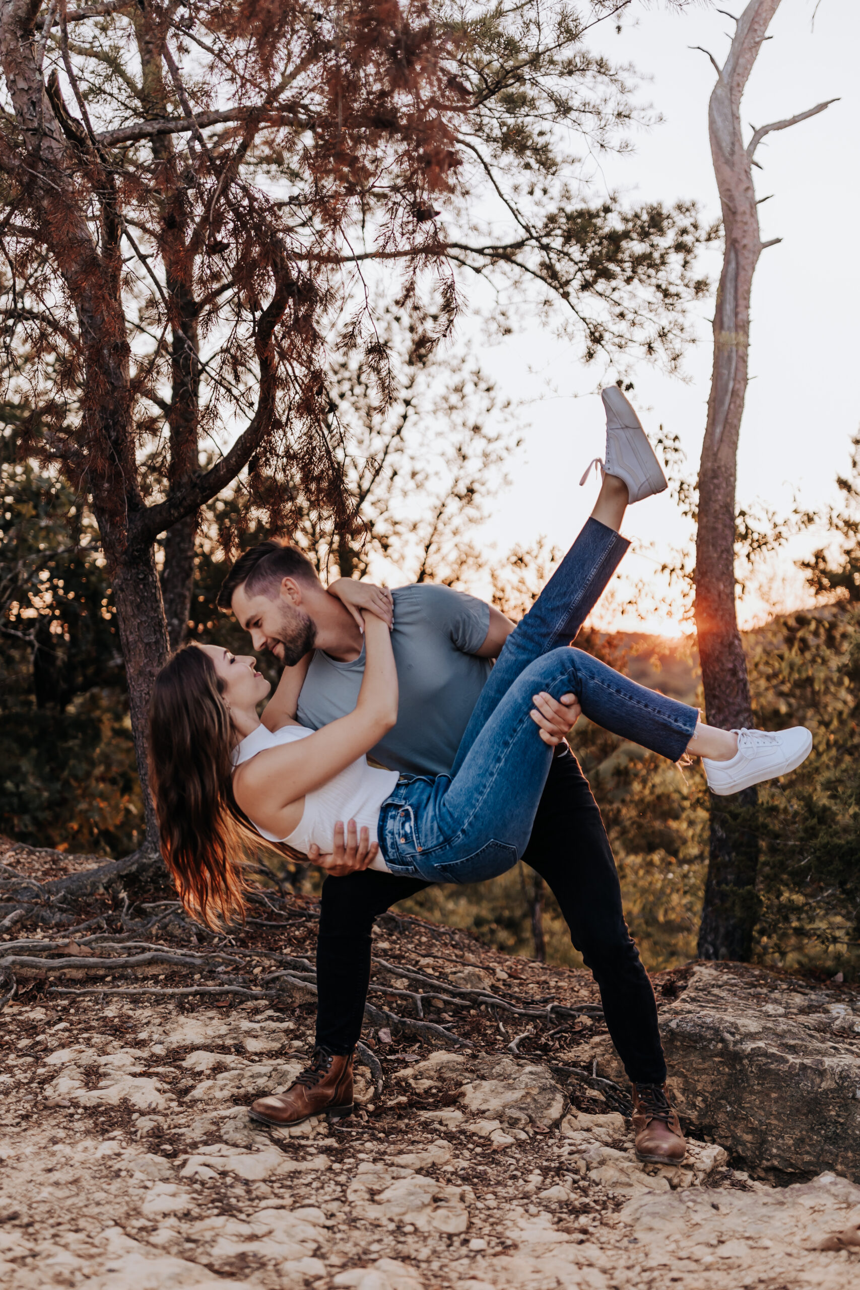 A couple shares a dramatic dip and kiss among tall trees at sunset, full of movement and playful romance, captured by a Nashville engagement photographer.