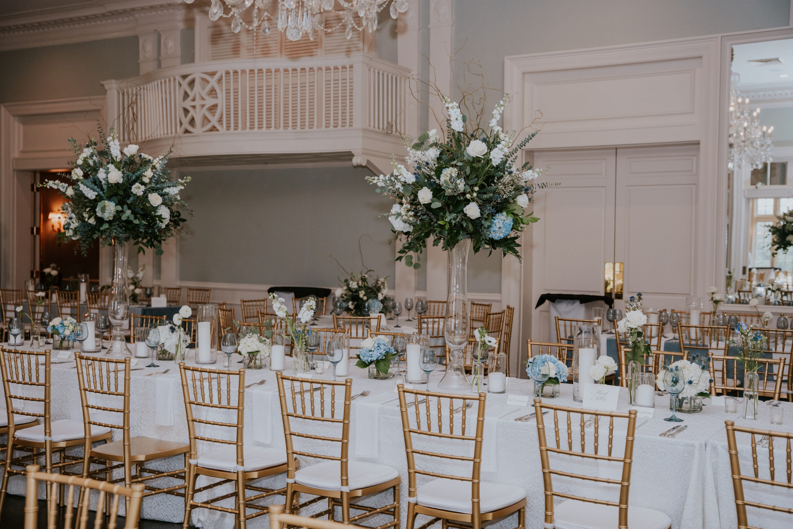 Chic reception tables lined with gold Chiavari chairs and lush white-and-blue floral centerpieces—event design details often featured in wedding photographer packages.