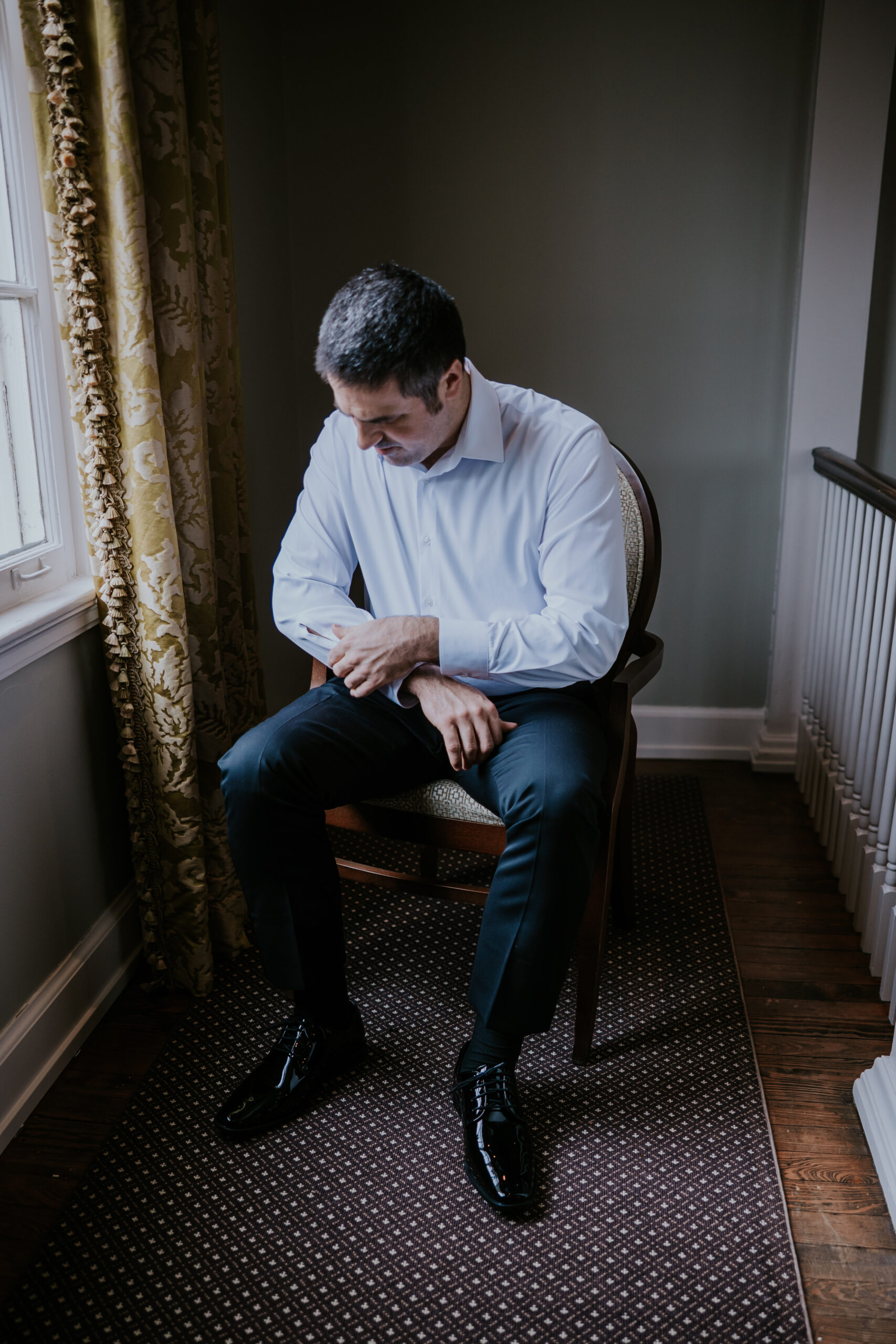 The groom fastens his cufflinks near a softly lit window, a thoughtful detail often highlighted in wedding photographer packages.