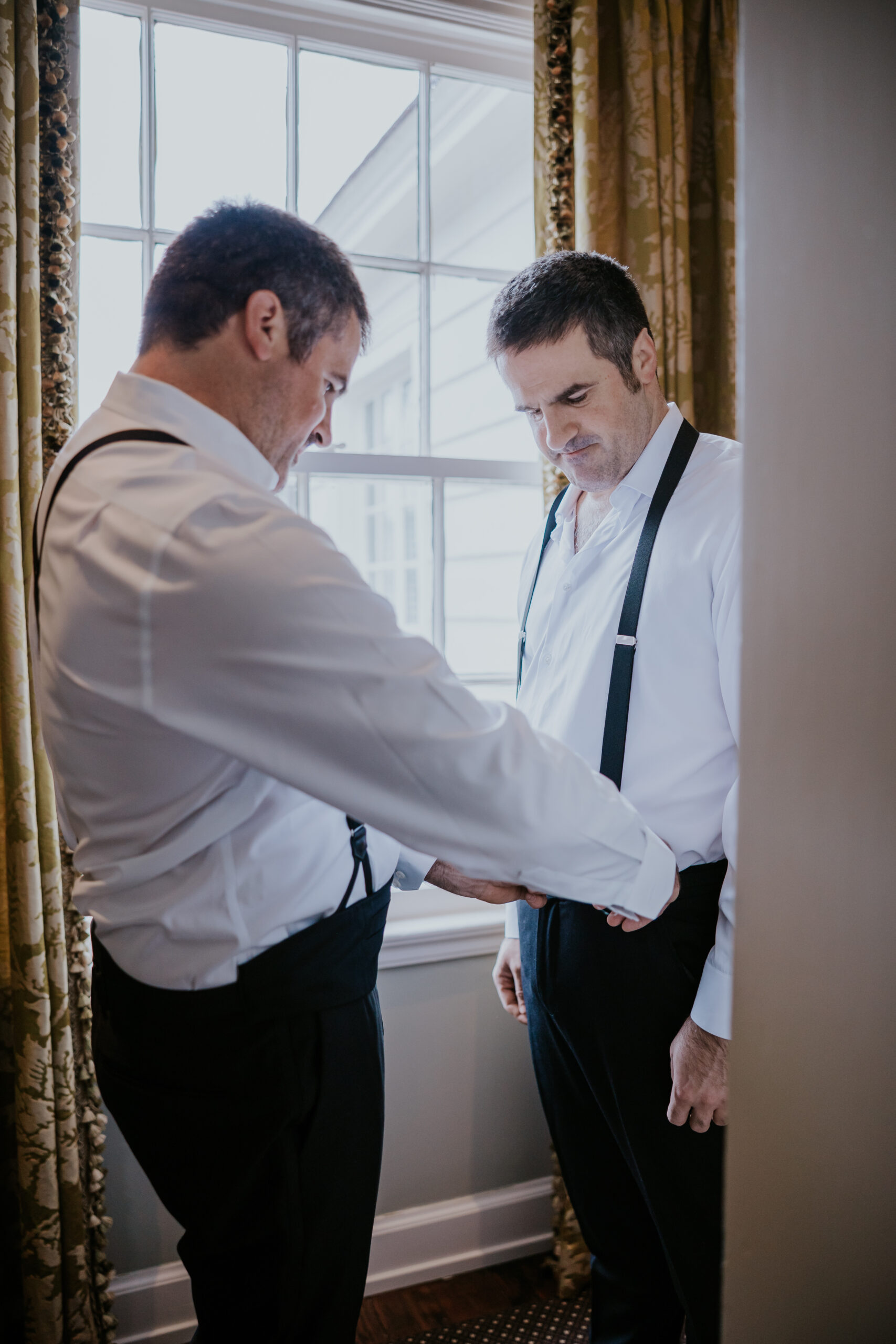 Candid shot of groomsmen helping the groom get dressed, a fun behind-the-scenes glimpse into wedding day prep.