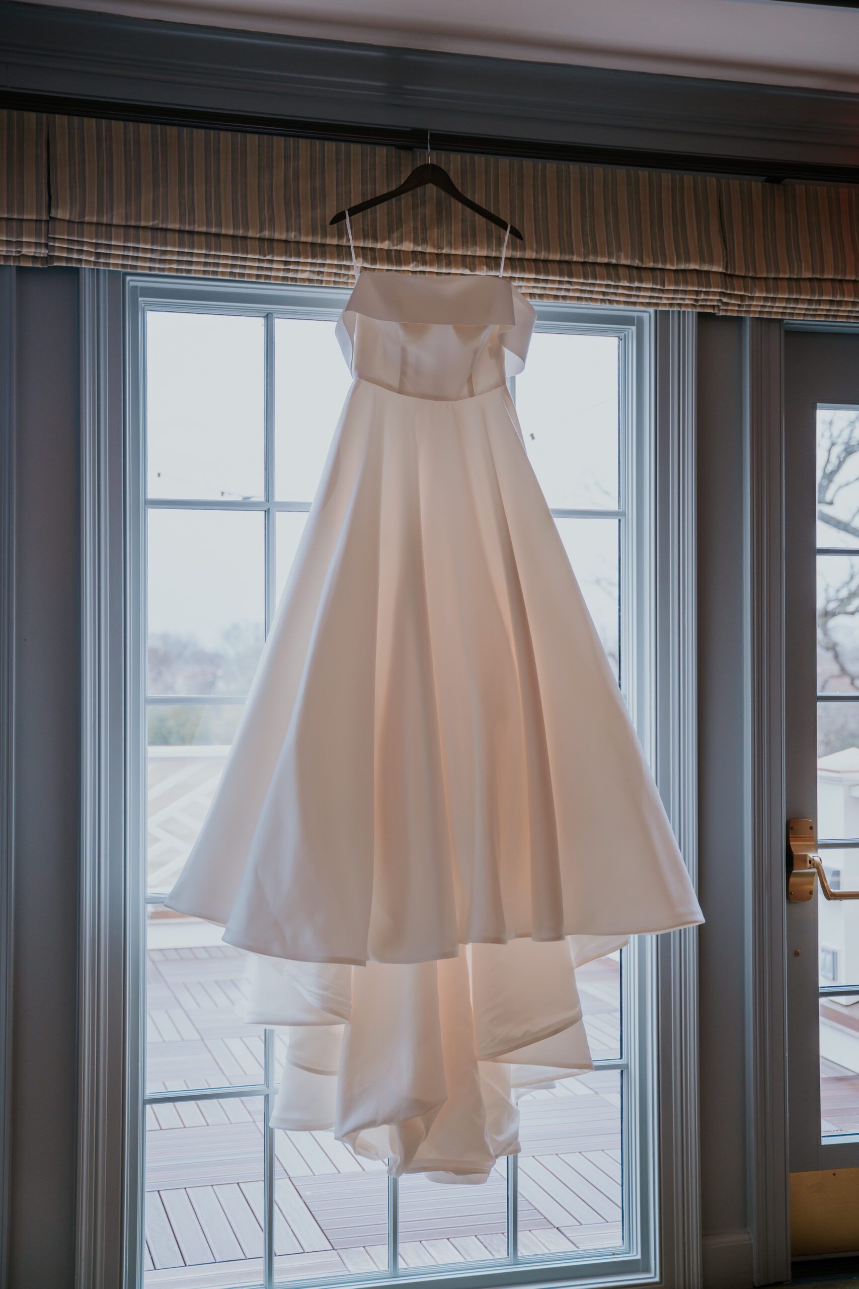 Classic white wedding dress on a hanger in front of French doors, a staple pre-ceremony shot included in most wedding photographer packages.