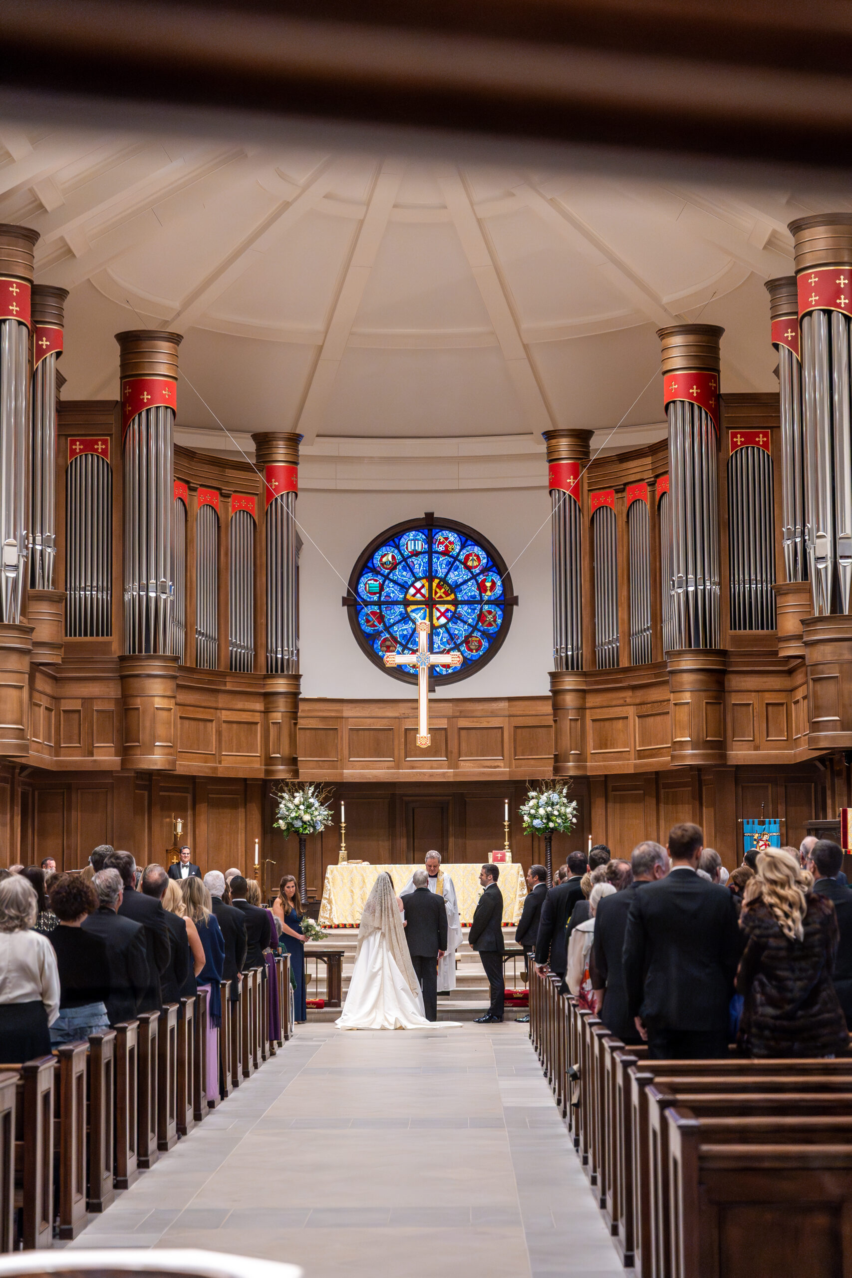 The couple stands at the altar beneath a stained-glass window and grand organ pipes during their church ceremony.
