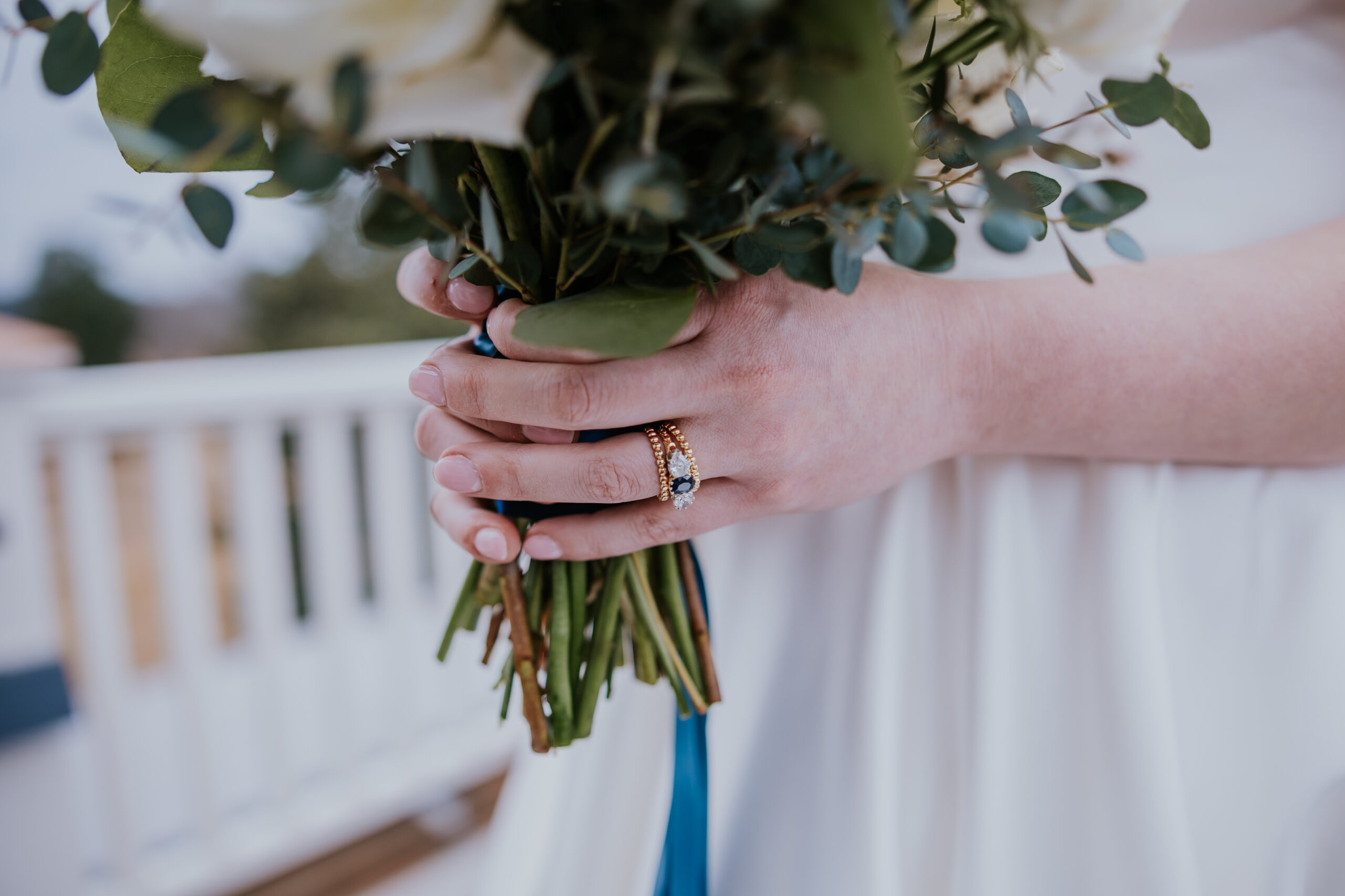 Detailed shot of the bride’s hands wrapped around her bouquet, highlighting her sapphire engagement ring and delicate gold wedding band.