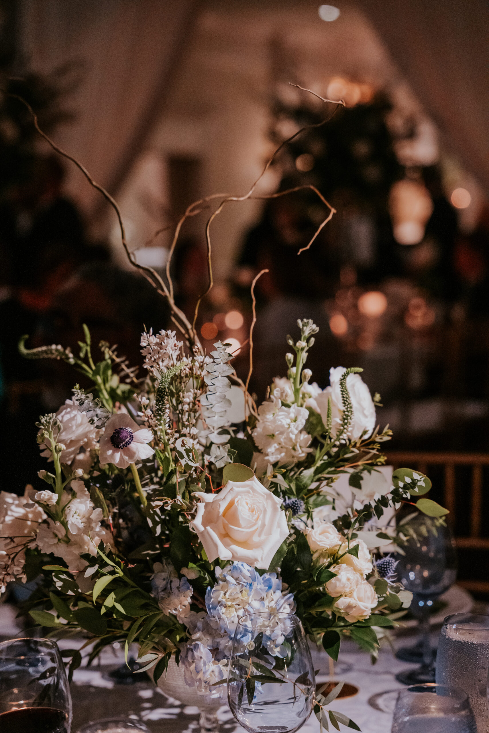 A romantic, low-lit centerpiece filled with roses, hydrangeas, and twigs sets the mood for an intimate evening.