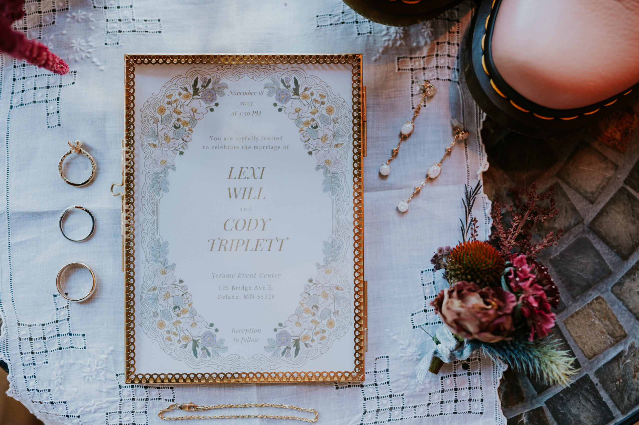 A flat lay of the wedding invitation suite with jewelry, rings, and a boutonnière at the couple’s wedding in Minnesota.