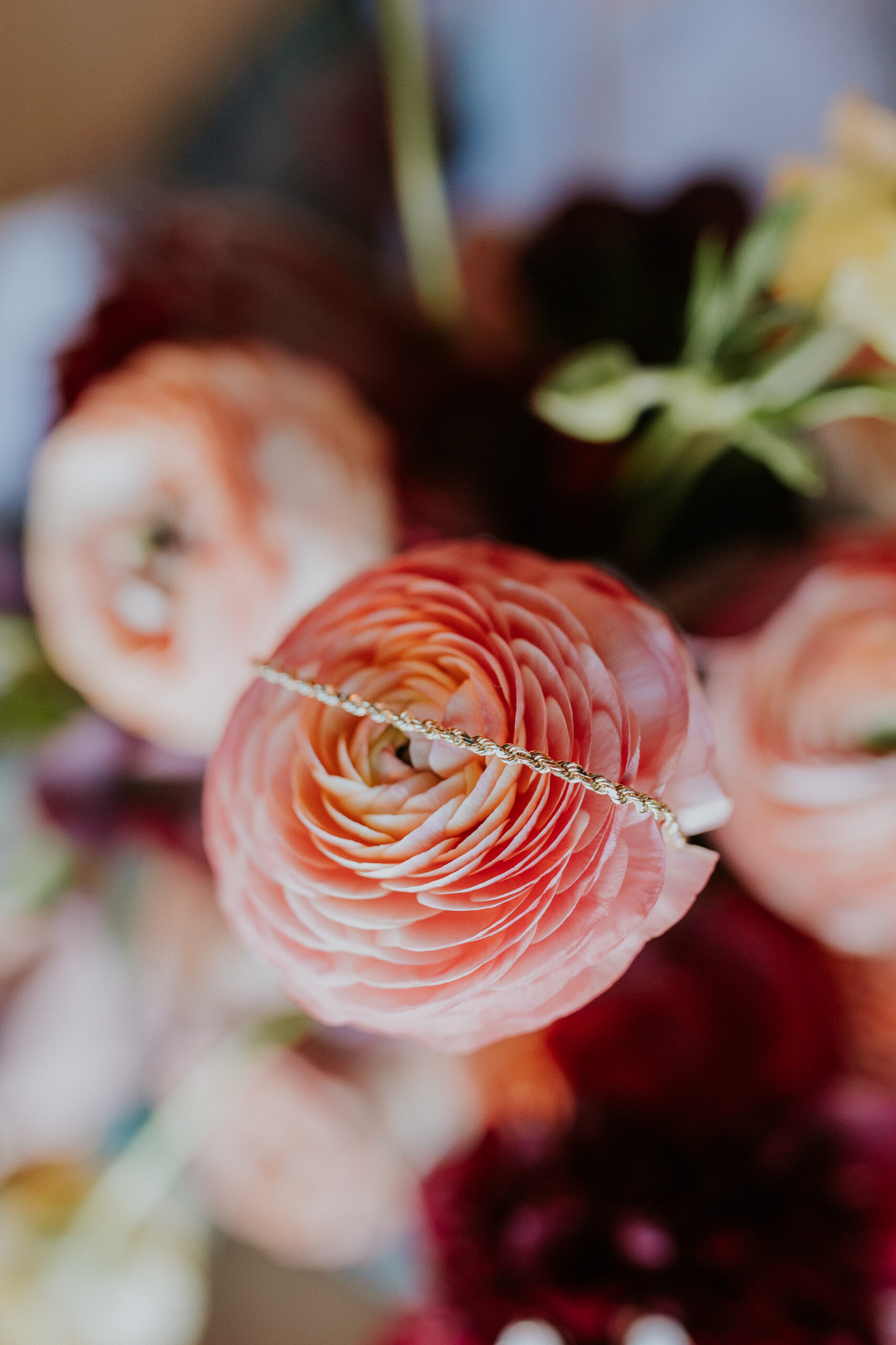 A delicate gold bracelet is draped over a fresh pink ranunculus bloom in the bride’s bouquet.