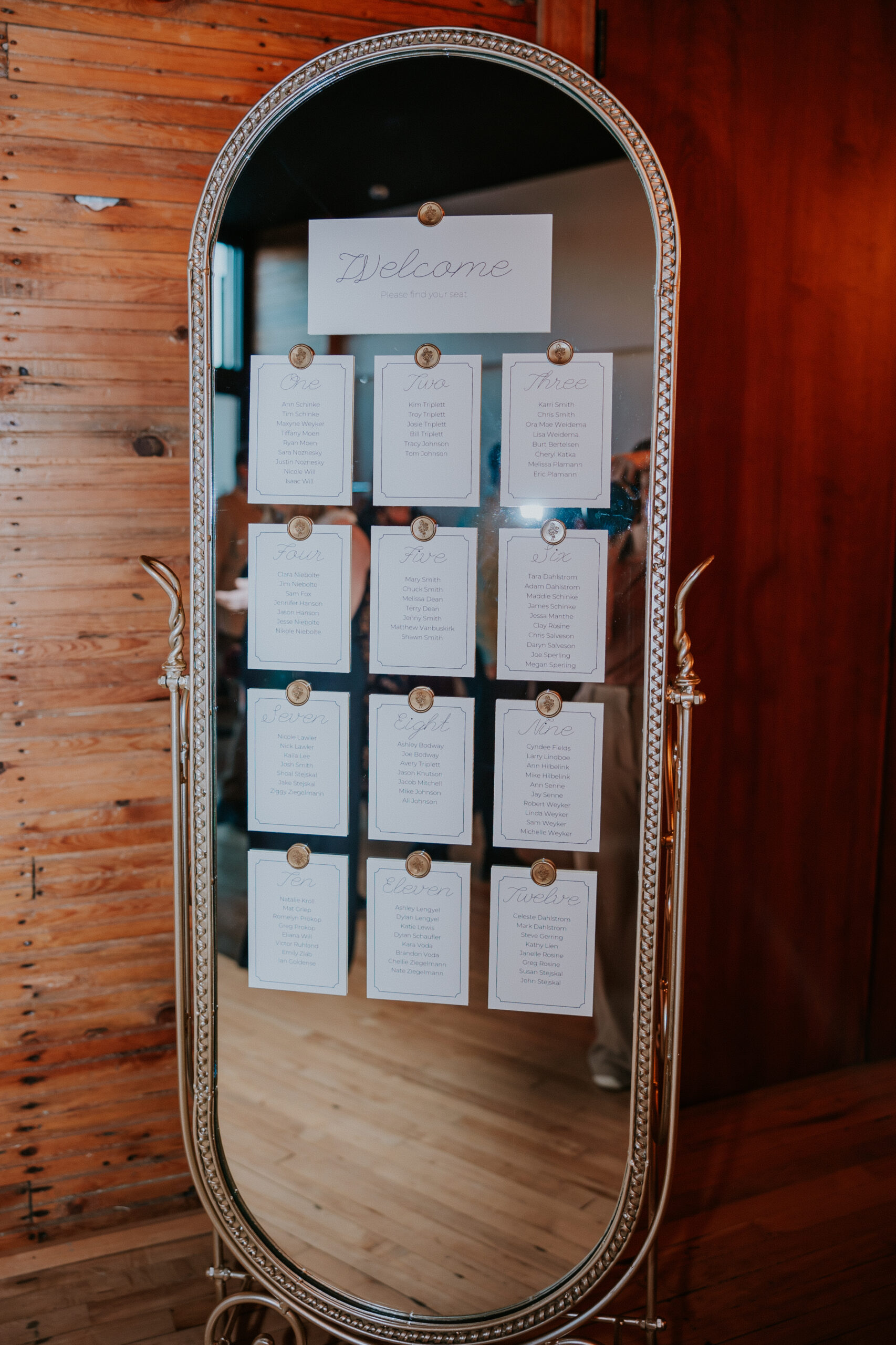 Elegant mirror seating chart decorated with calligraphy place cards and gold accents at a wedding in Minnesota.