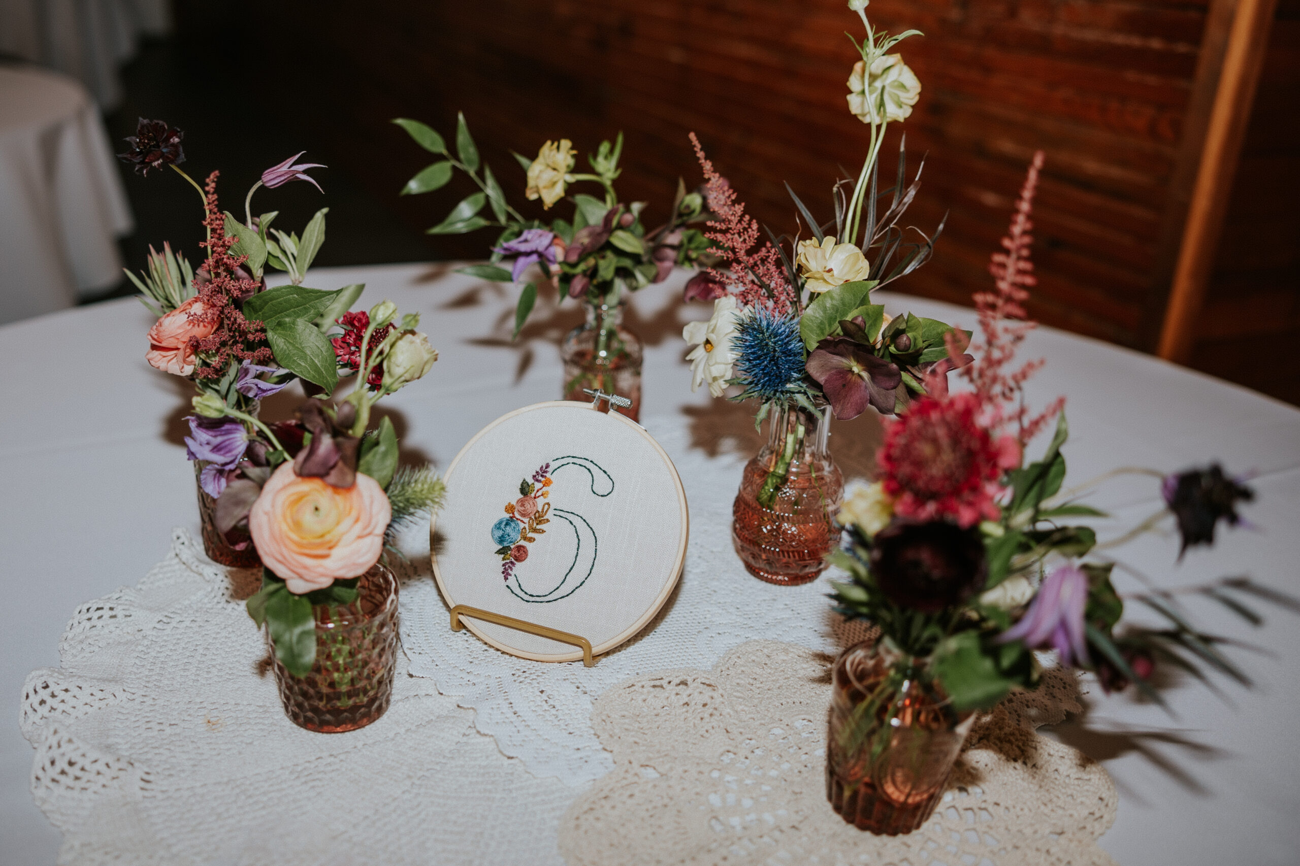 Whimsical floral centerpieces with a custom embroidered table number displayed on a lace tablecloth at a wedding reception.