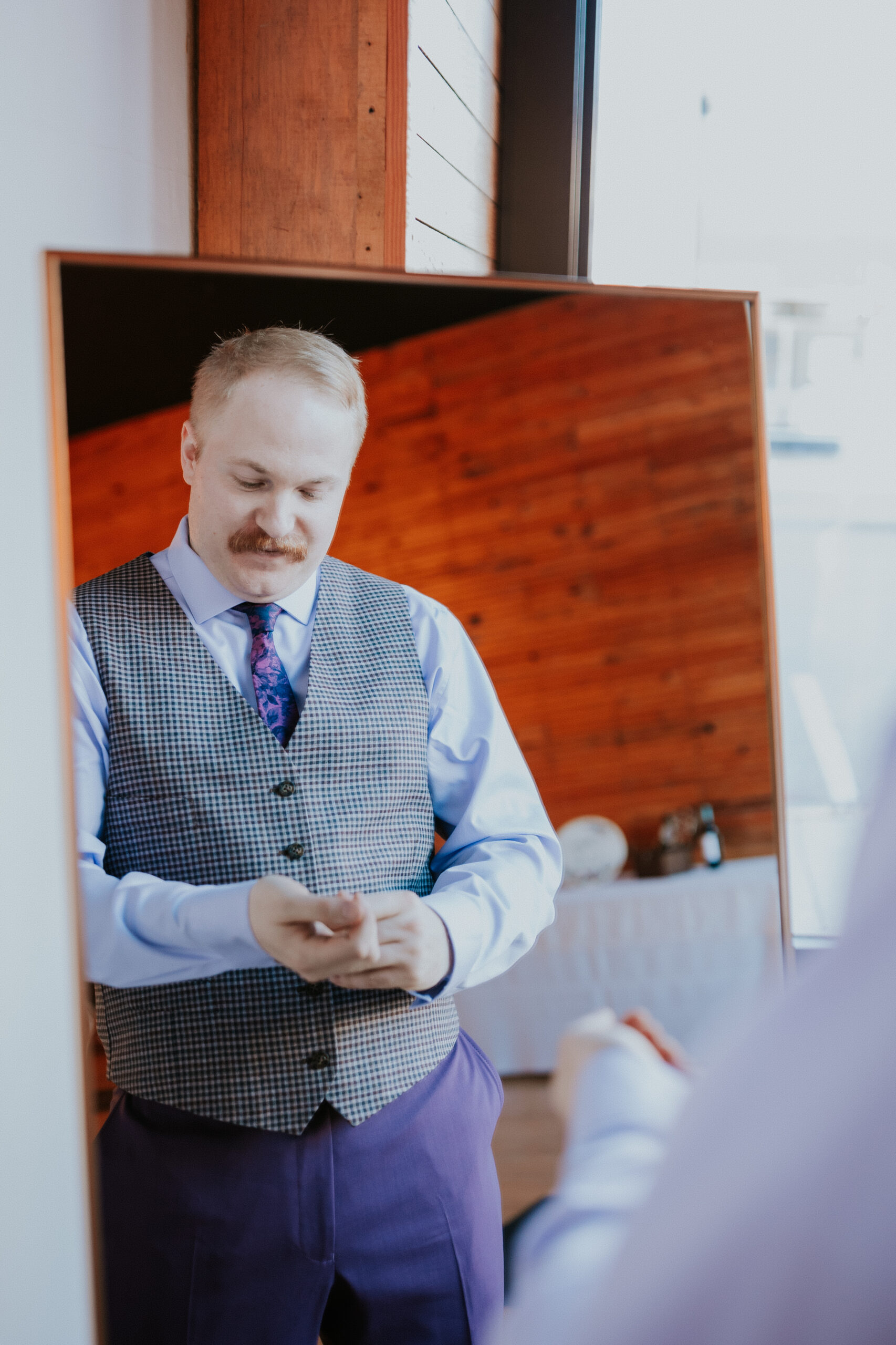 The groom stands in front of a mirror, adjusting his cufflinks and preparing for the wedding in Minnesota.