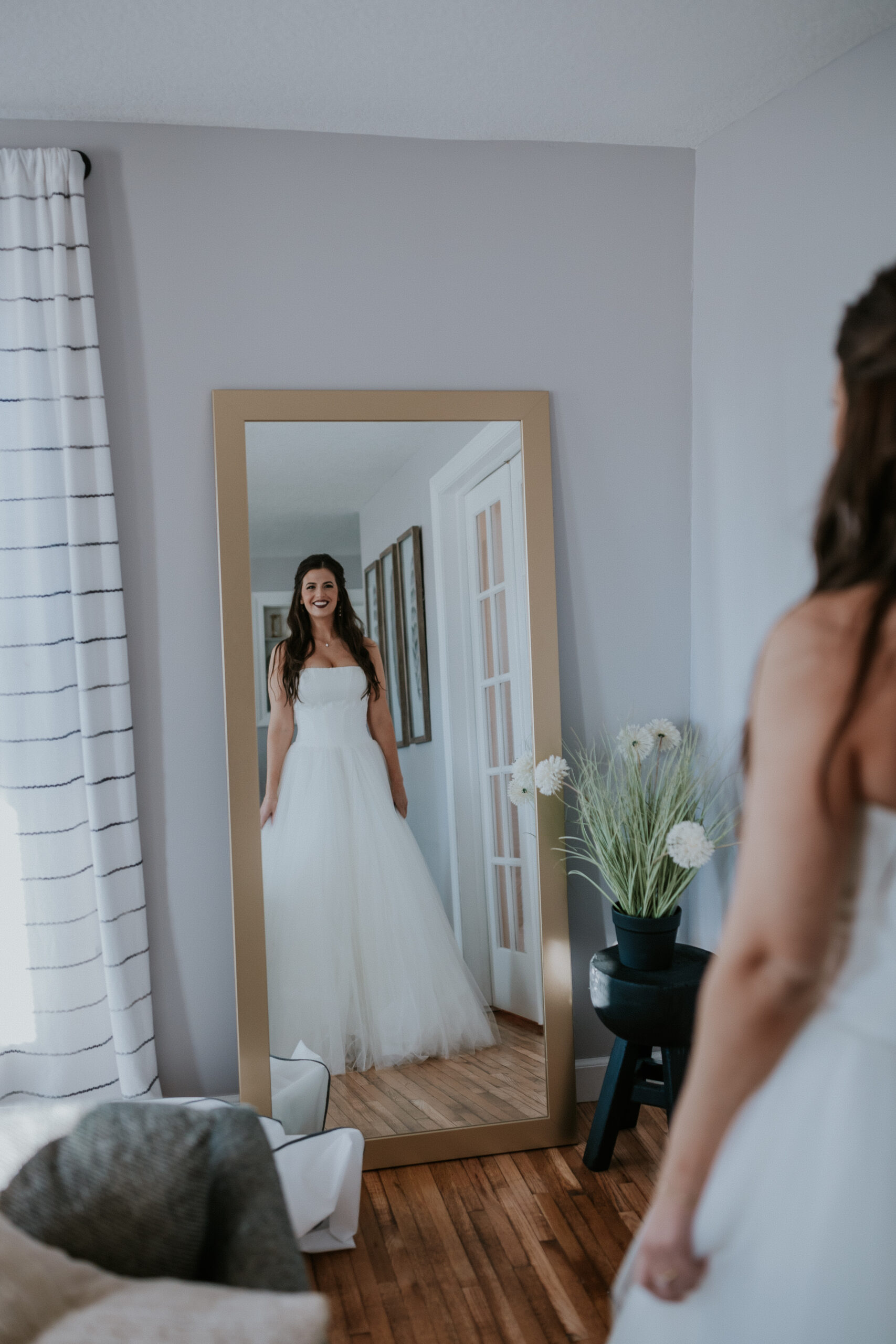 The bride admires her full look in the mirror, glowing with excitement on her wedding day in Minnesota.