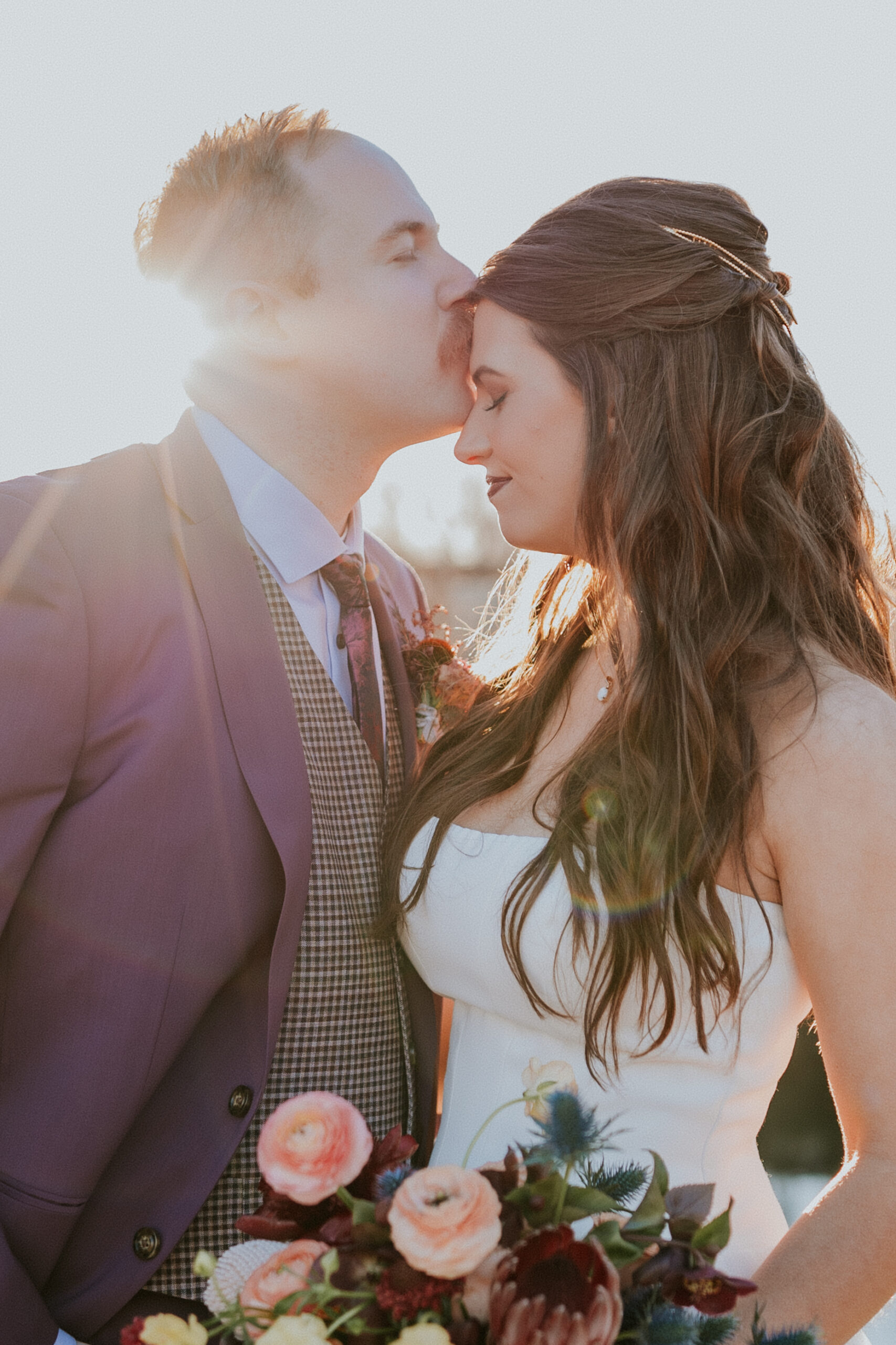 Golden hour moment of the groom kissing the bride’s forehead while holding her close during their wedding in Minnesota.