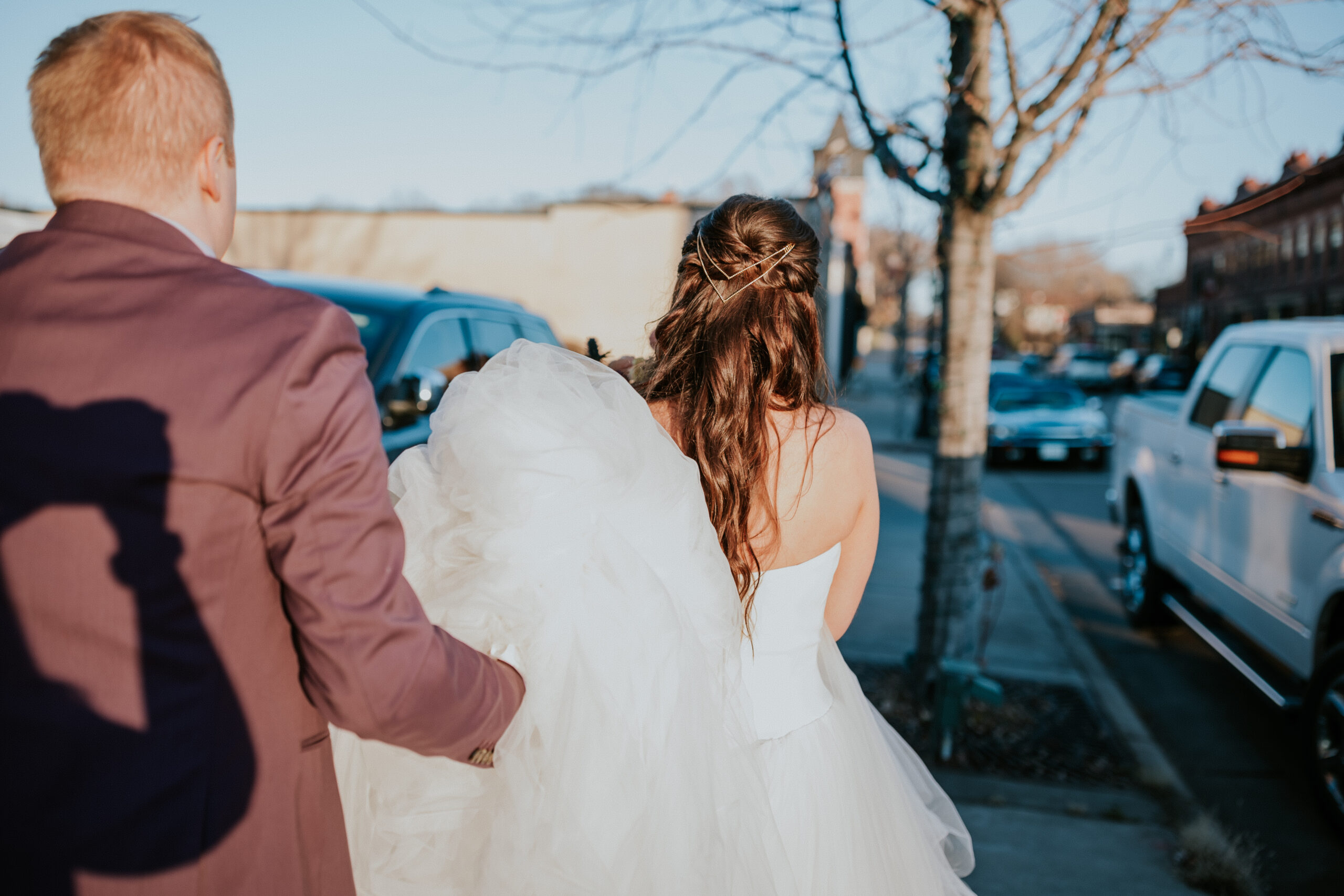 The couple walks down a downtown sidewalk, the bride’s gown trailing behind as they make their way hand in hand.