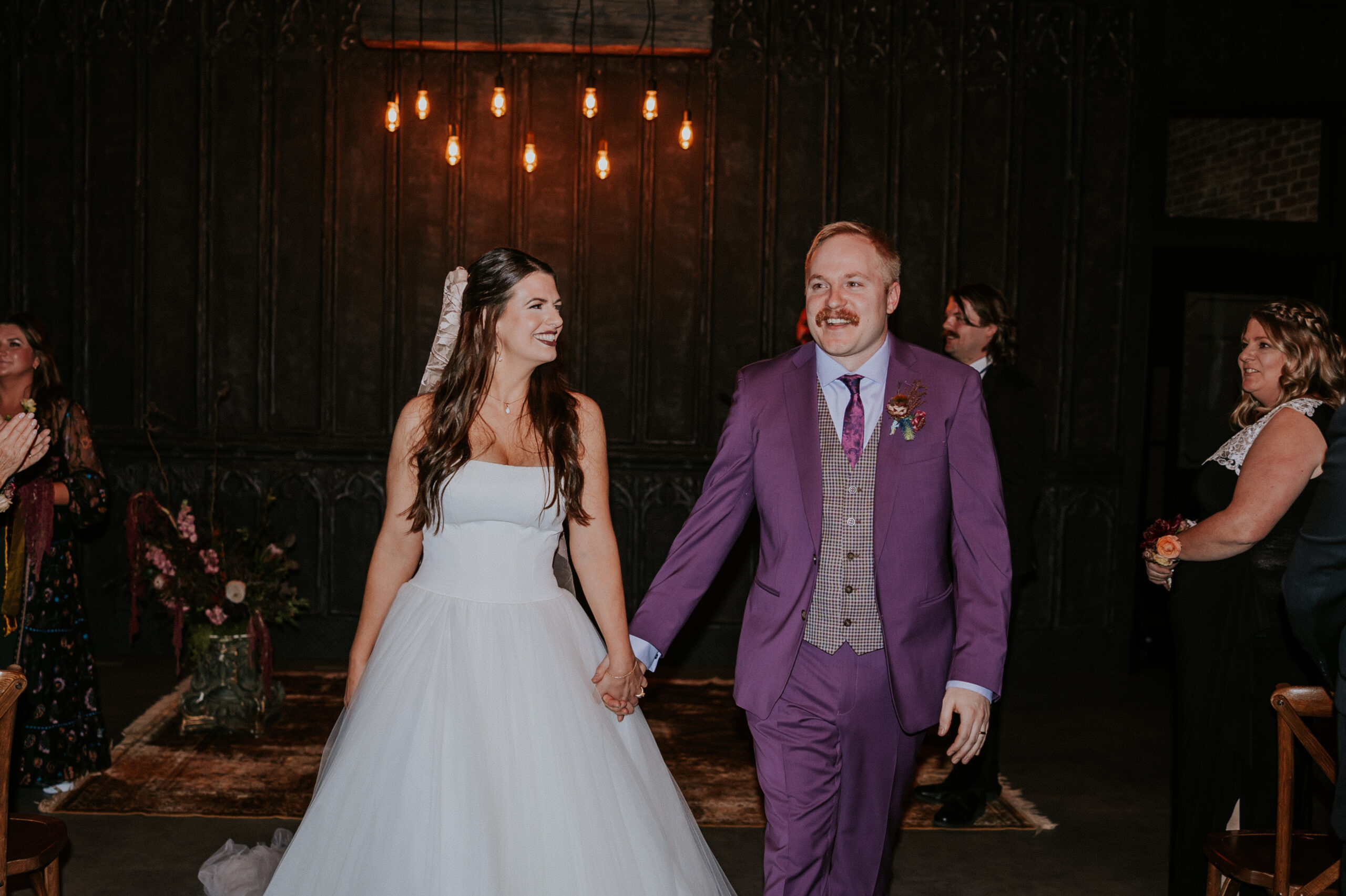 Newlyweds walk hand in hand back down the aisle, smiling at each other after saying “I do” at their wedding in Minnesota.