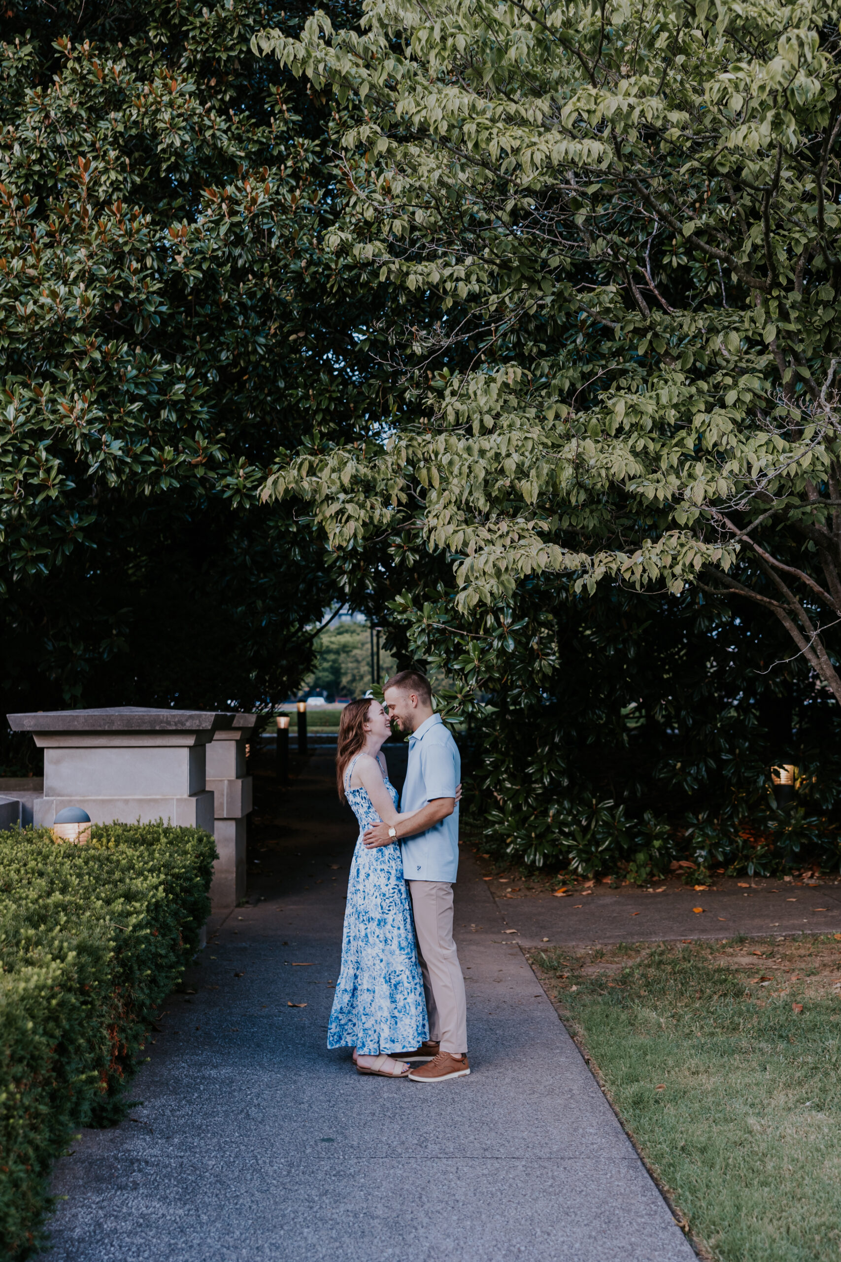 The couple shares an intimate moment in a quiet garden path, wearing matching light blue outfits — a stylish option for what to wear for engagement photos.
